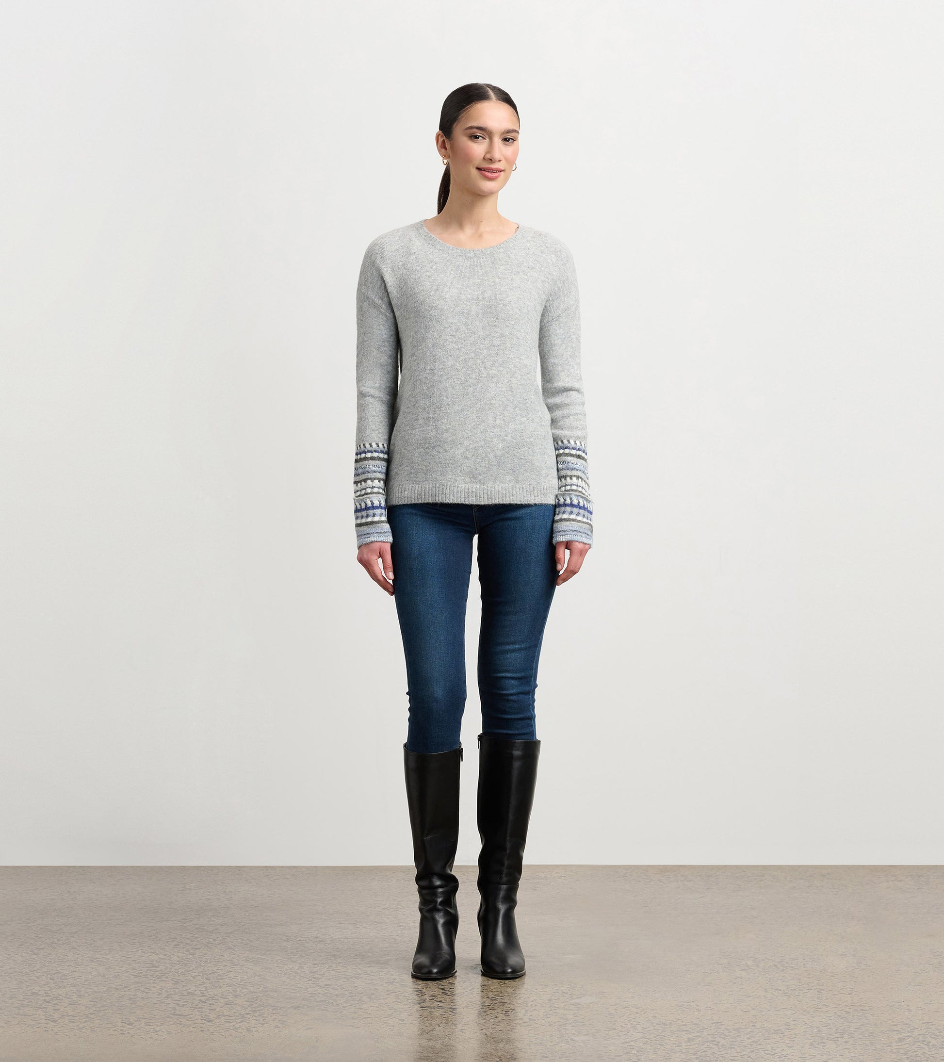 Grey melange sweater with patterned cuffs, featuring a crew neckline and long sleeves, styled with fitted jeans and boots.