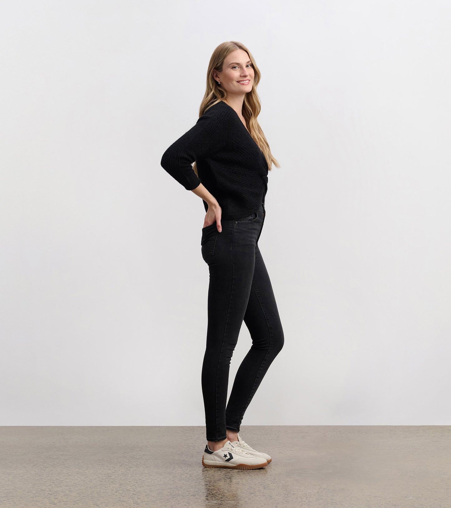 Black crossover sweater with three-quarter sleeves, styled with fitted black jeans and casual sneakers.