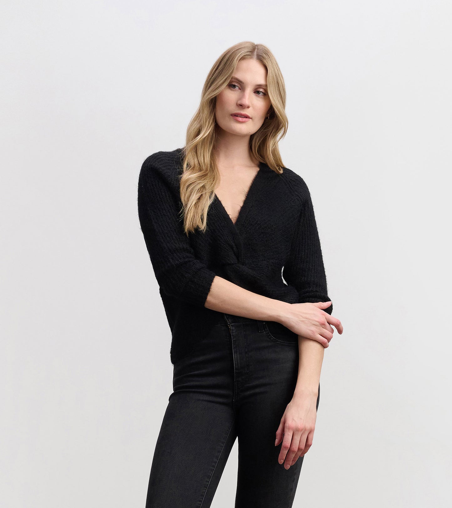 Black crossover sweater with a textured finish and three-quarter sleeves, styled with high-waisted jeans.