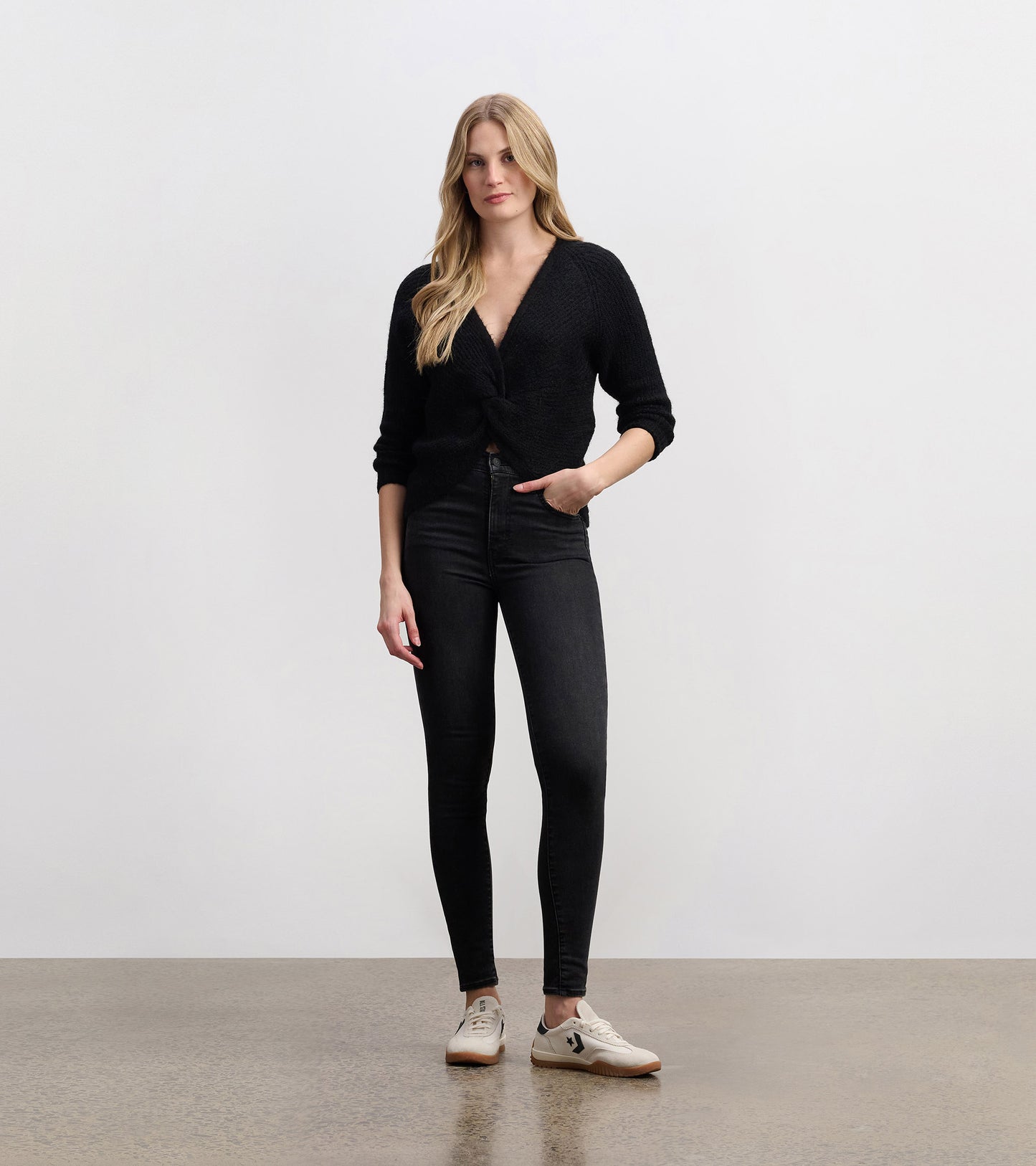 Black crossover sweater with a textured finish, featuring a deep V-neck and three-quarter sleeves, styled with skinny jeans.