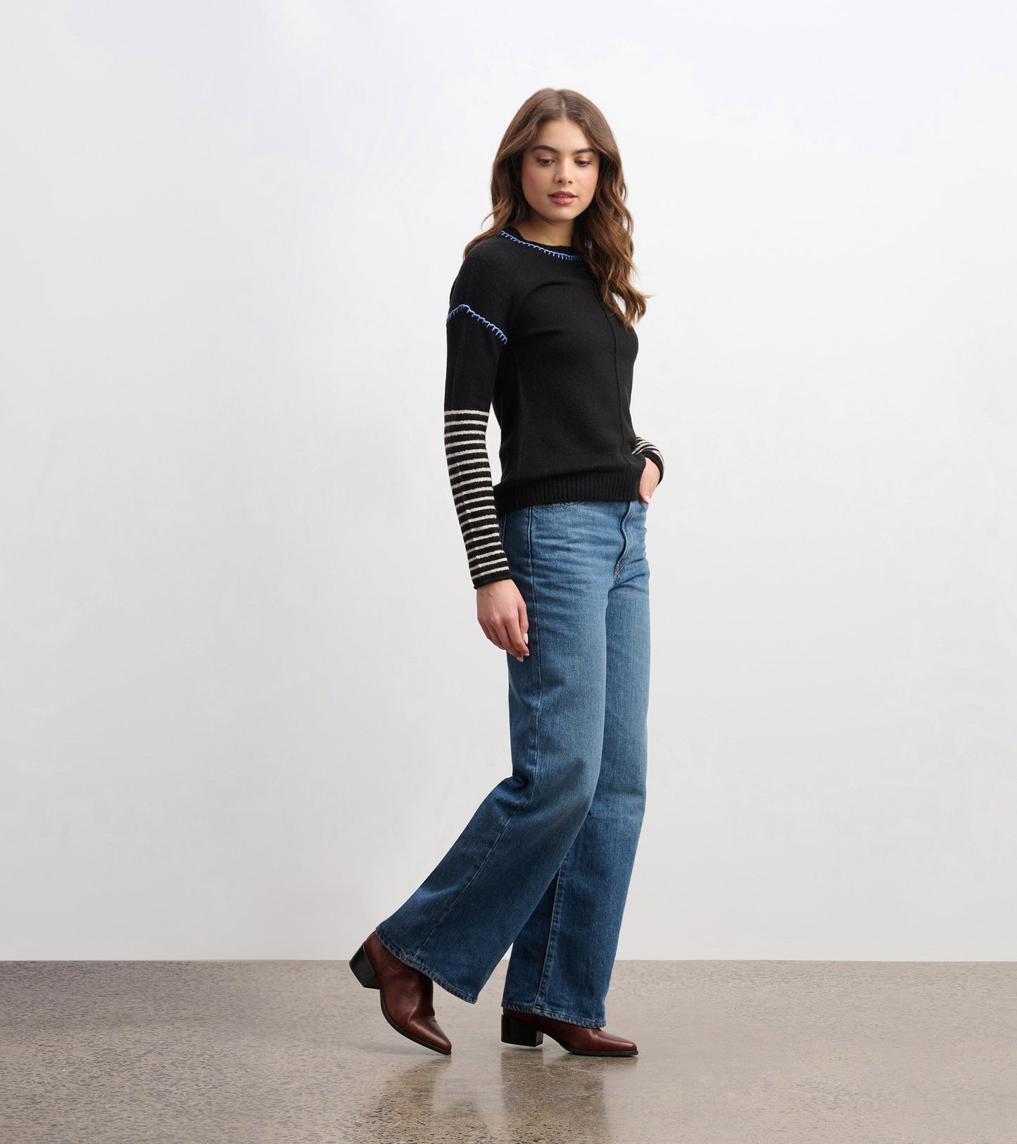 Black sweater with striped sleeves, paired with blue jeans and brown heeled boots, shown from the side.