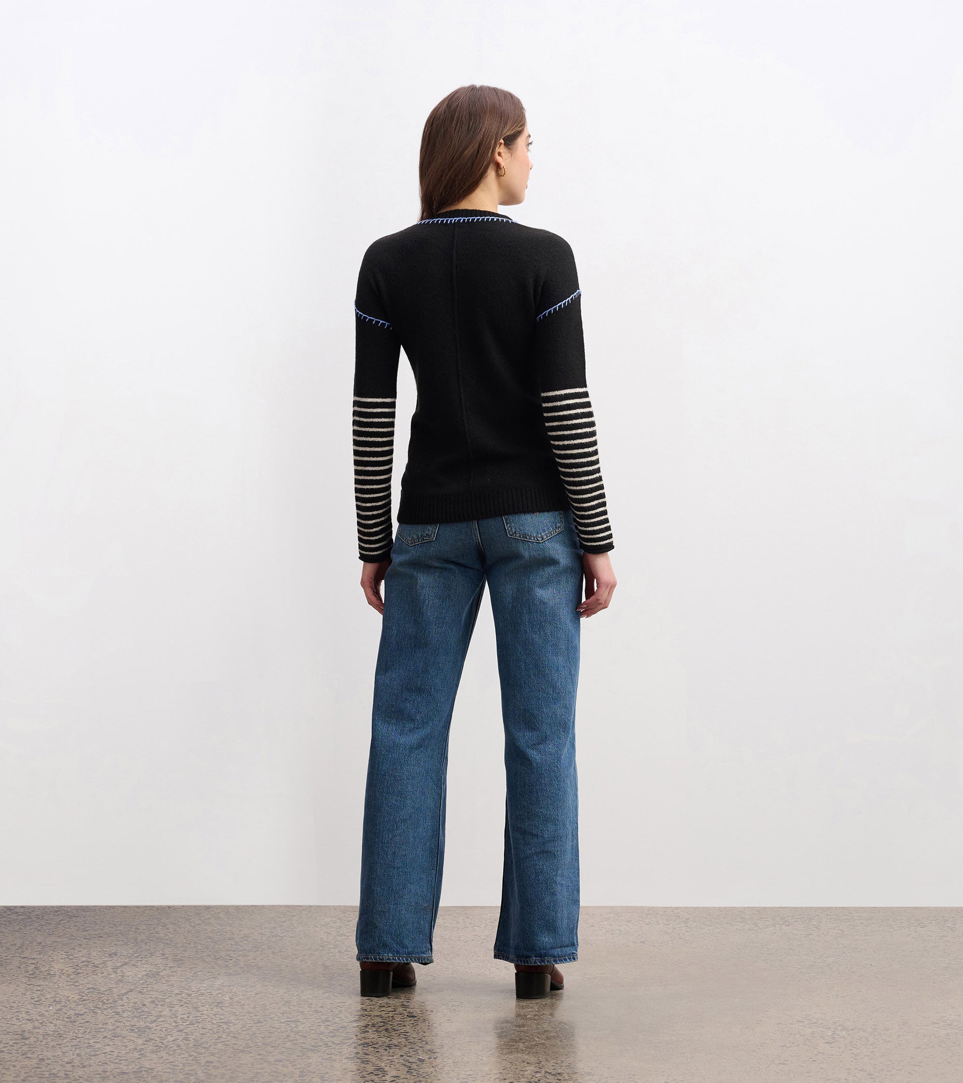 Black sweater with striped sleeves, fitted shape, and a round neckline, worn with blue jeans, viewed from the back.