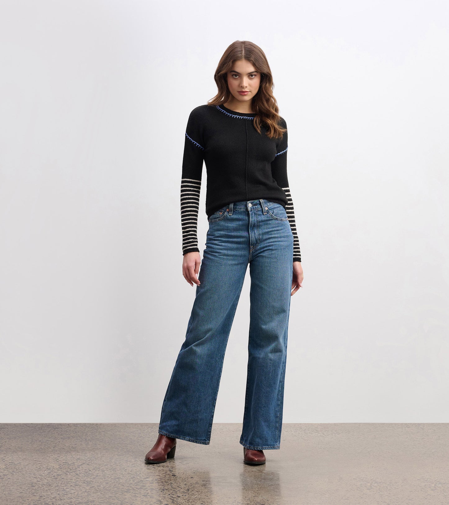 Black sweater with striped sleeves and blue stitching, paired with high-waisted jeans and heeled boots.