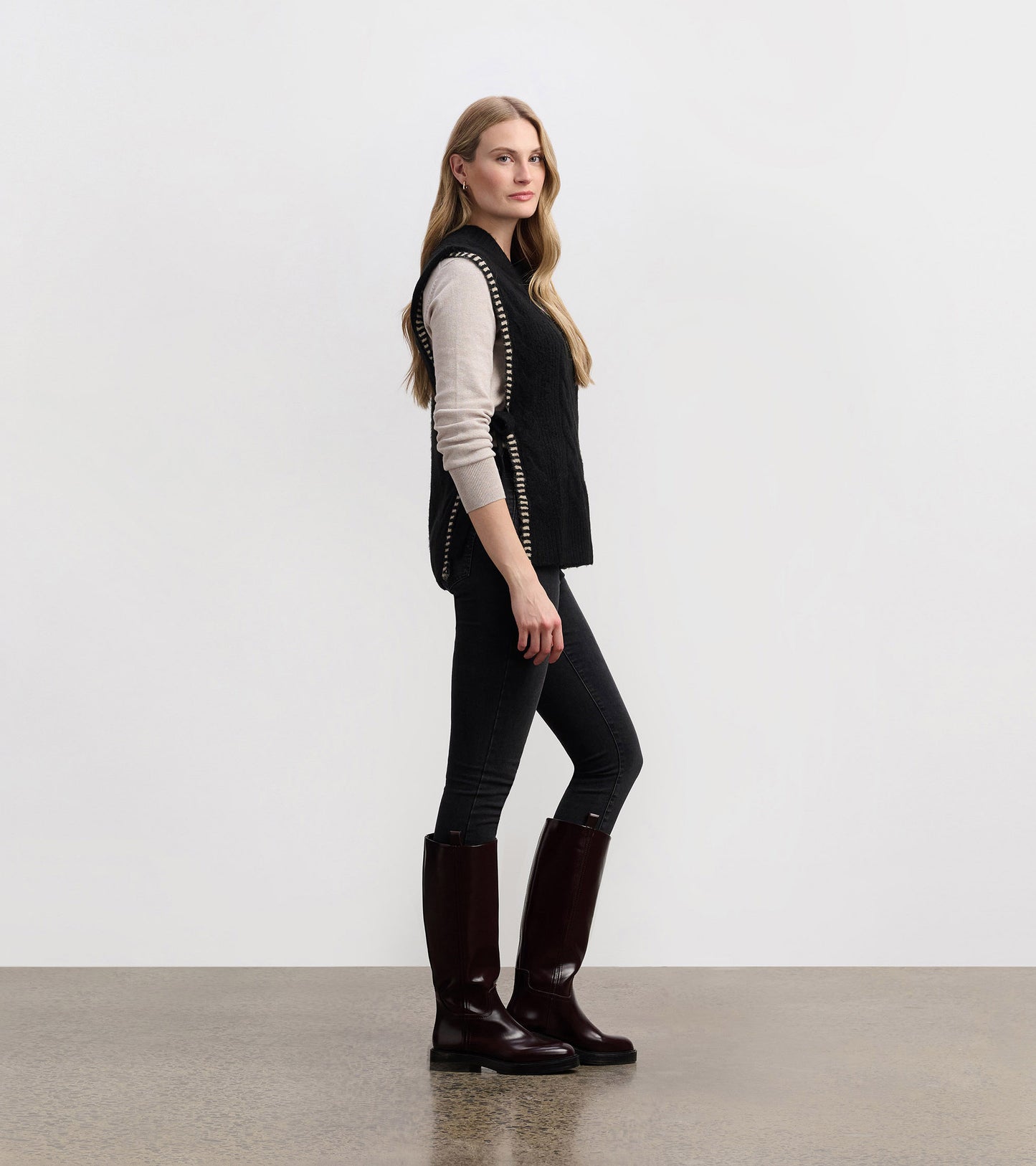 Black side-tie sweater vest with a textured pattern, styled over a light top and paired with dark jeans and knee-high boots.