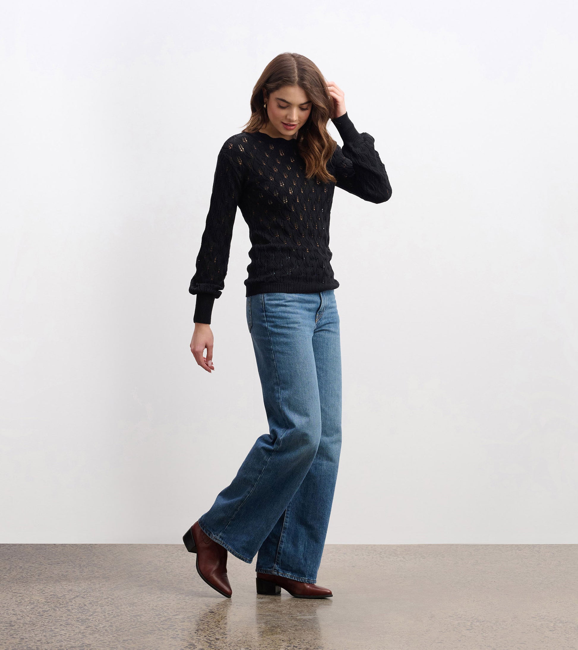 Black knitted sweater with a textured pattern, featuring long sleeves and a round neckline, styled with blue jeans.