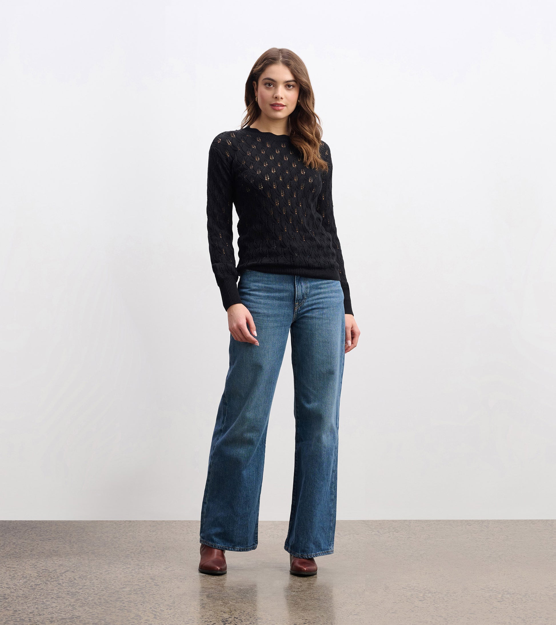 Black knitted sweater with a textured pattern, featuring long sleeves and a round neckline, styled with blue jeans.