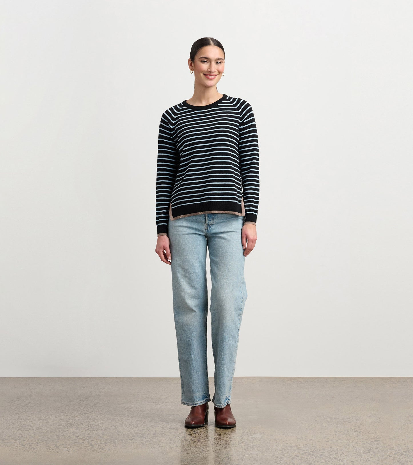 Black sweater with denim stripes, crew neck, long sleeves, paired with light blue jeans and brown boots.