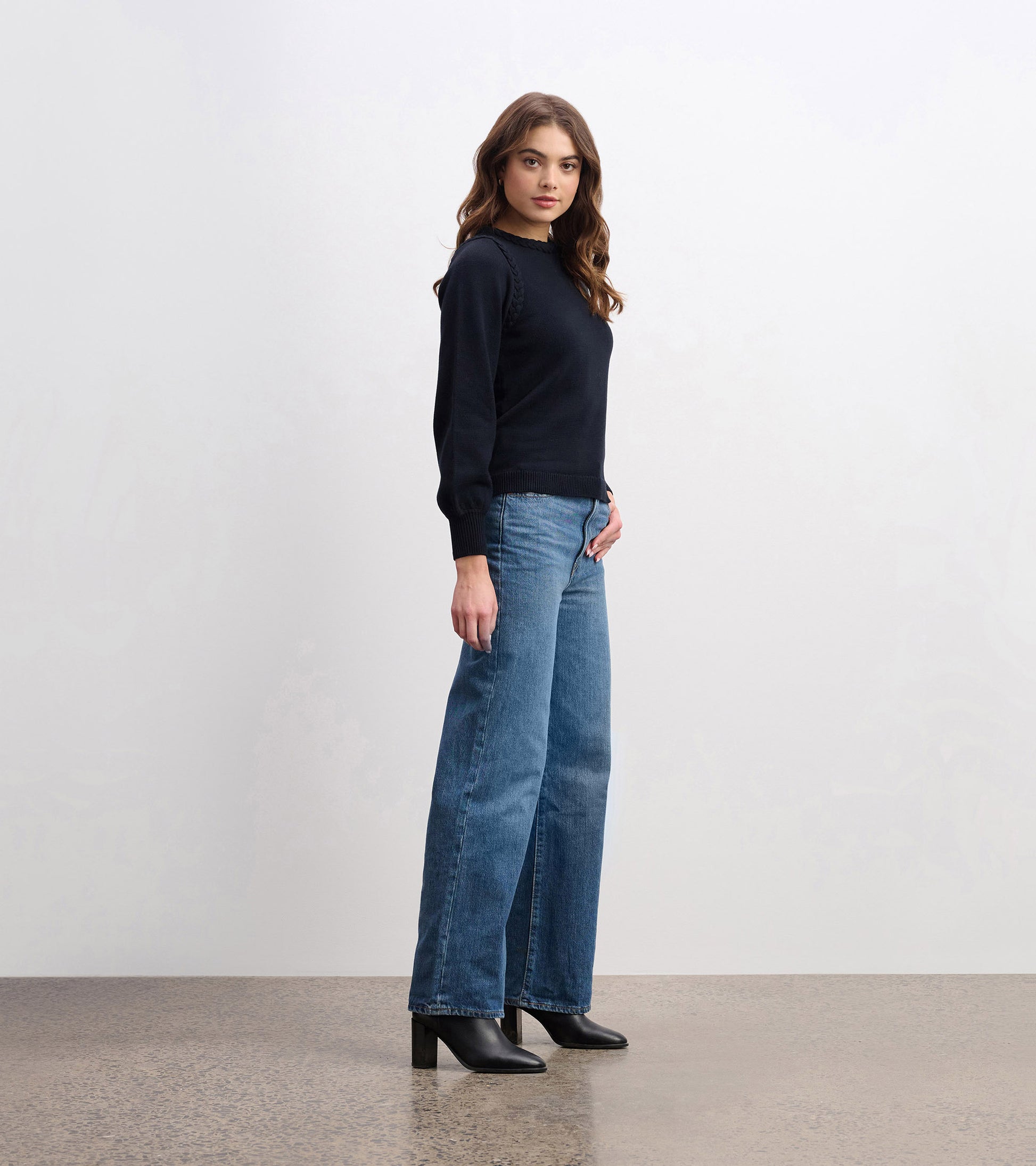 Black braided sweater with long sleeves, paired with wide-leg jeans and ankle boots, styled for a casual look.
