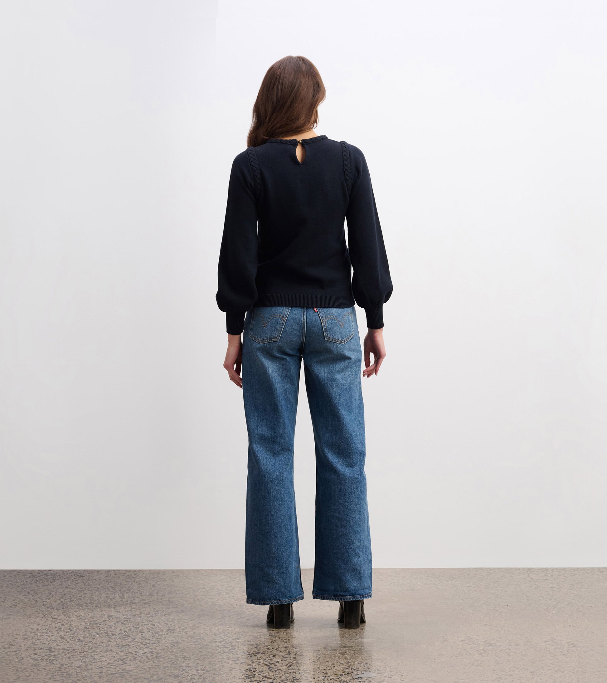 Black braided sweater with a keyhole back detail, paired with wide-leg jeans, viewed from the back.