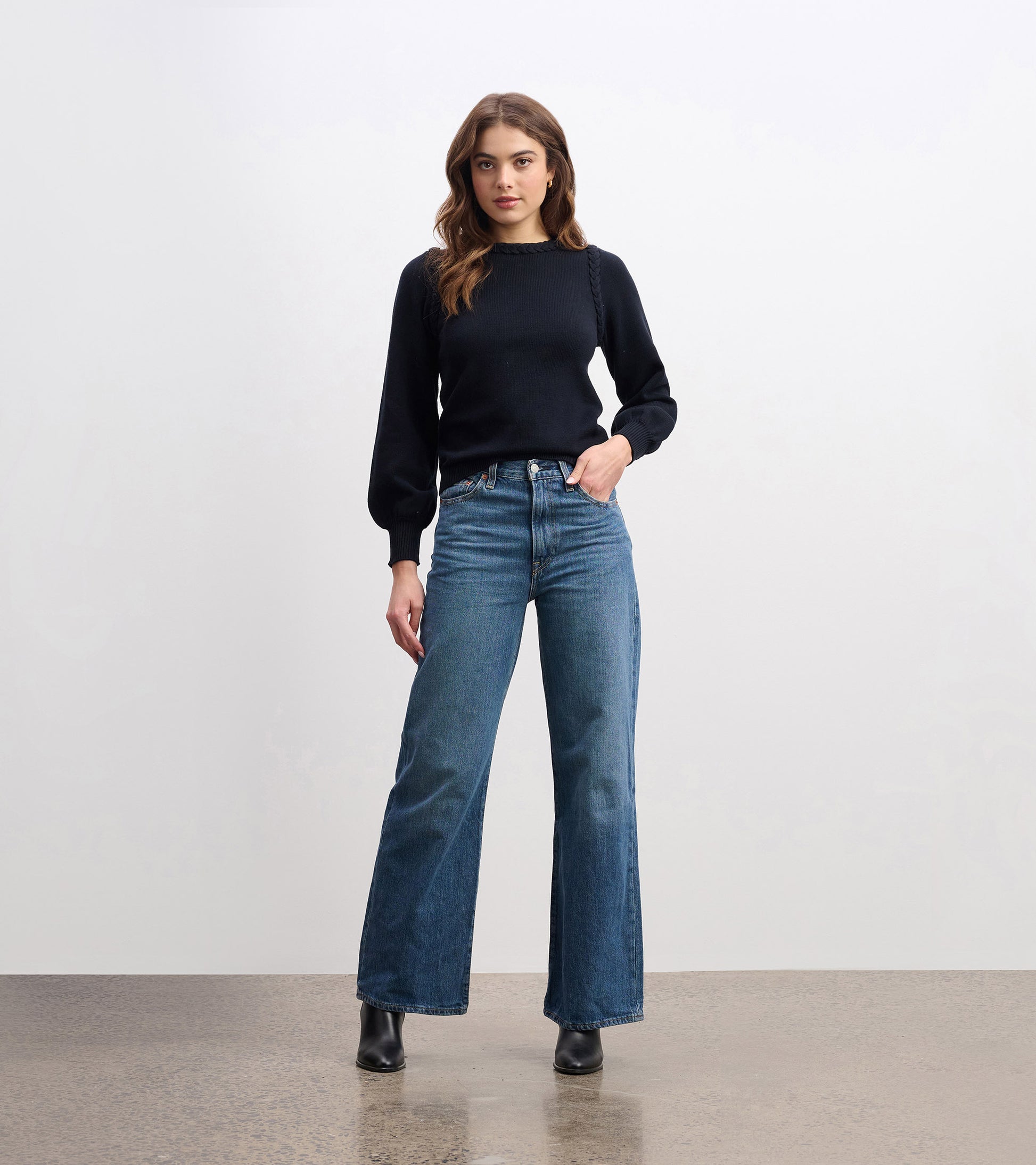 Black braided sweater with long sleeves, styled with high-waisted blue jeans and ankle boots.