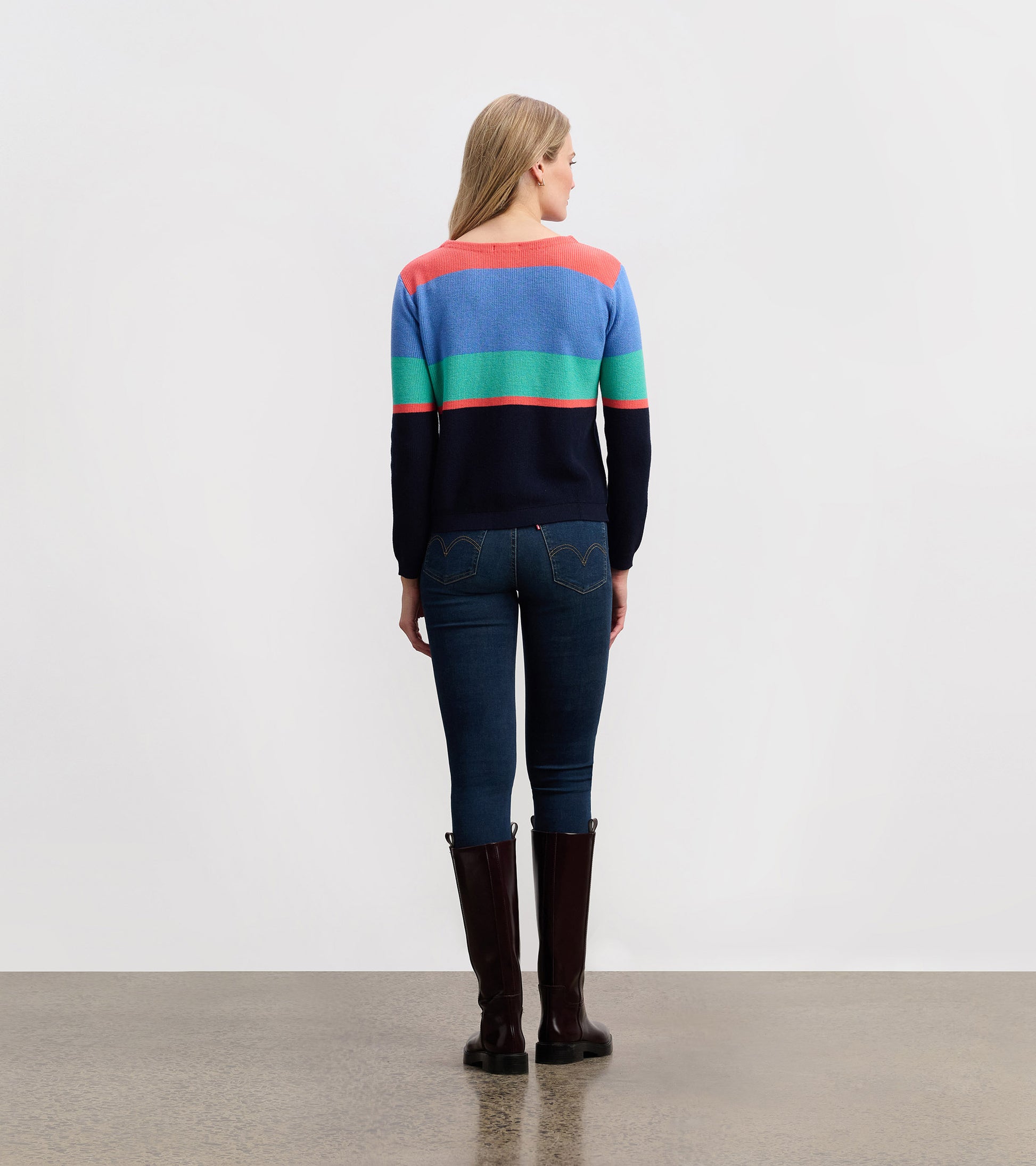 Bright colorblock striped sweater featuring blue, green, coral, and navy colors, styled with fitted jeans and tall boots.