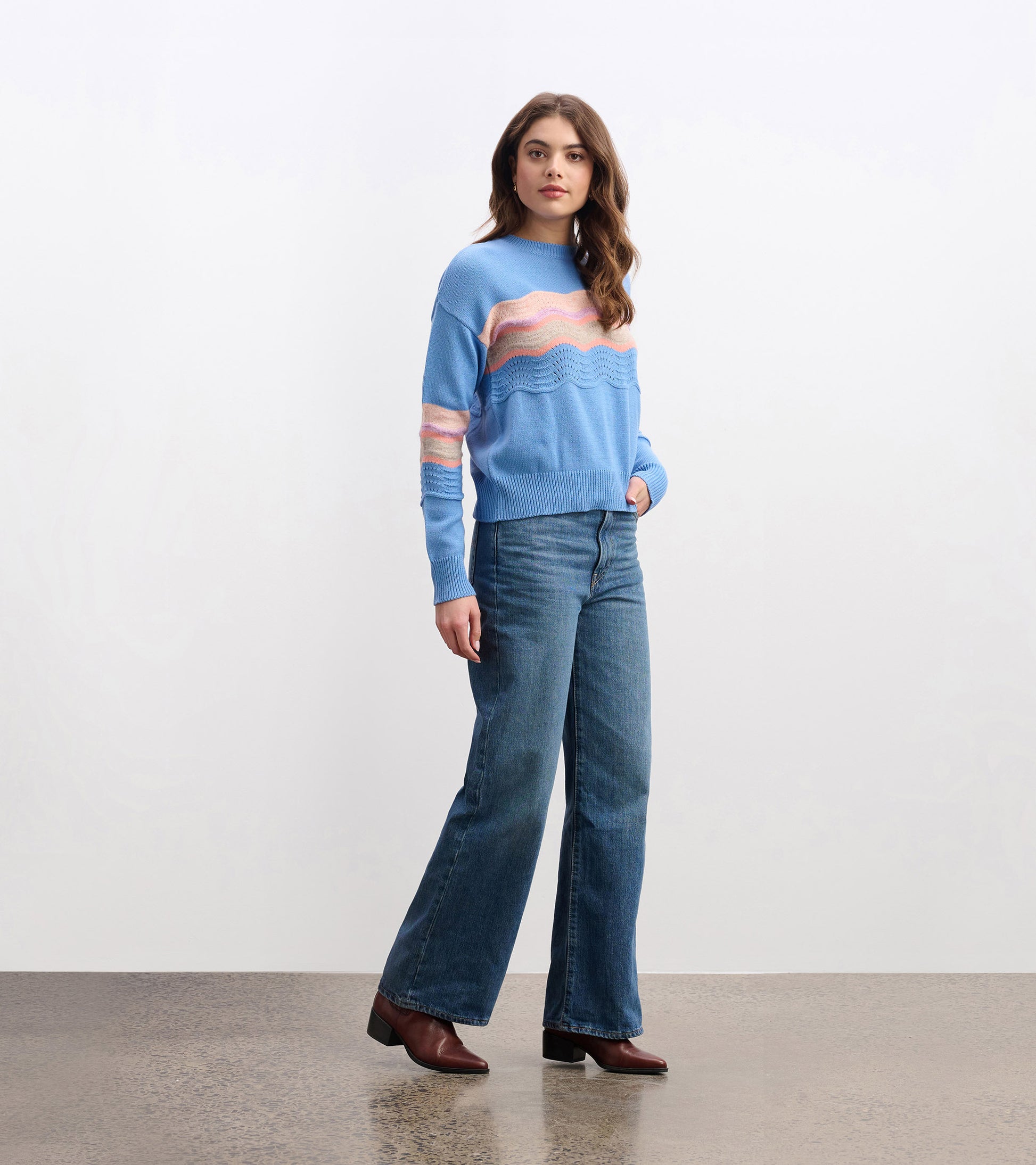 Sky blue sweater featuring a wavy pattern in pink and white, paired with high-waisted jeans and ankle boots.
