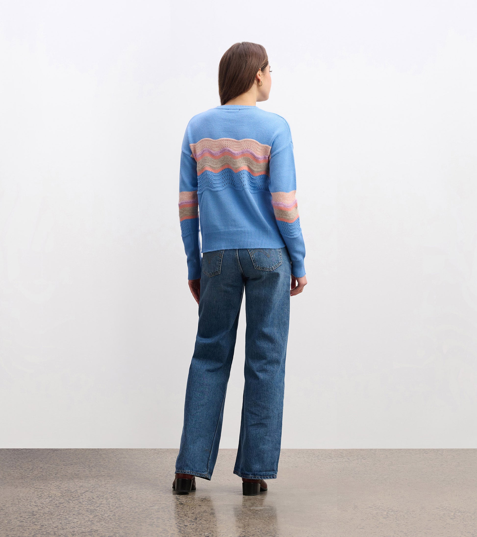 Sky blue sweater featuring a wave pattern in pink and cream, styled with relaxed-fit jeans.