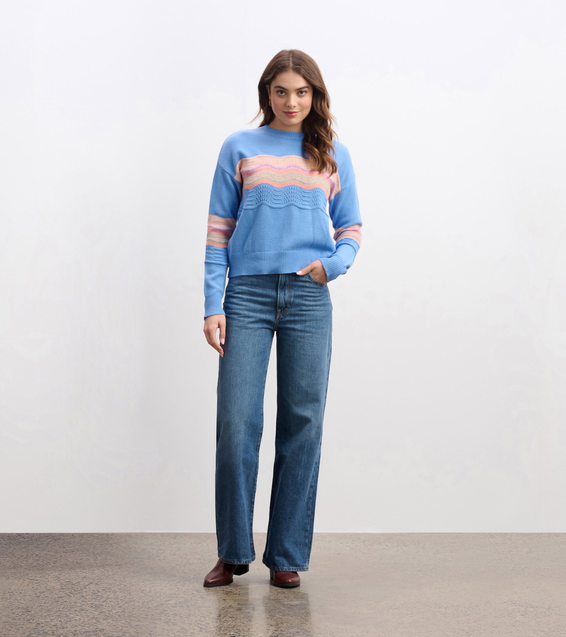 Sky blue sweater with wave pattern in pink and cream, featuring a relaxed fit and ribbed cuffs, paired with wide-leg jeans.