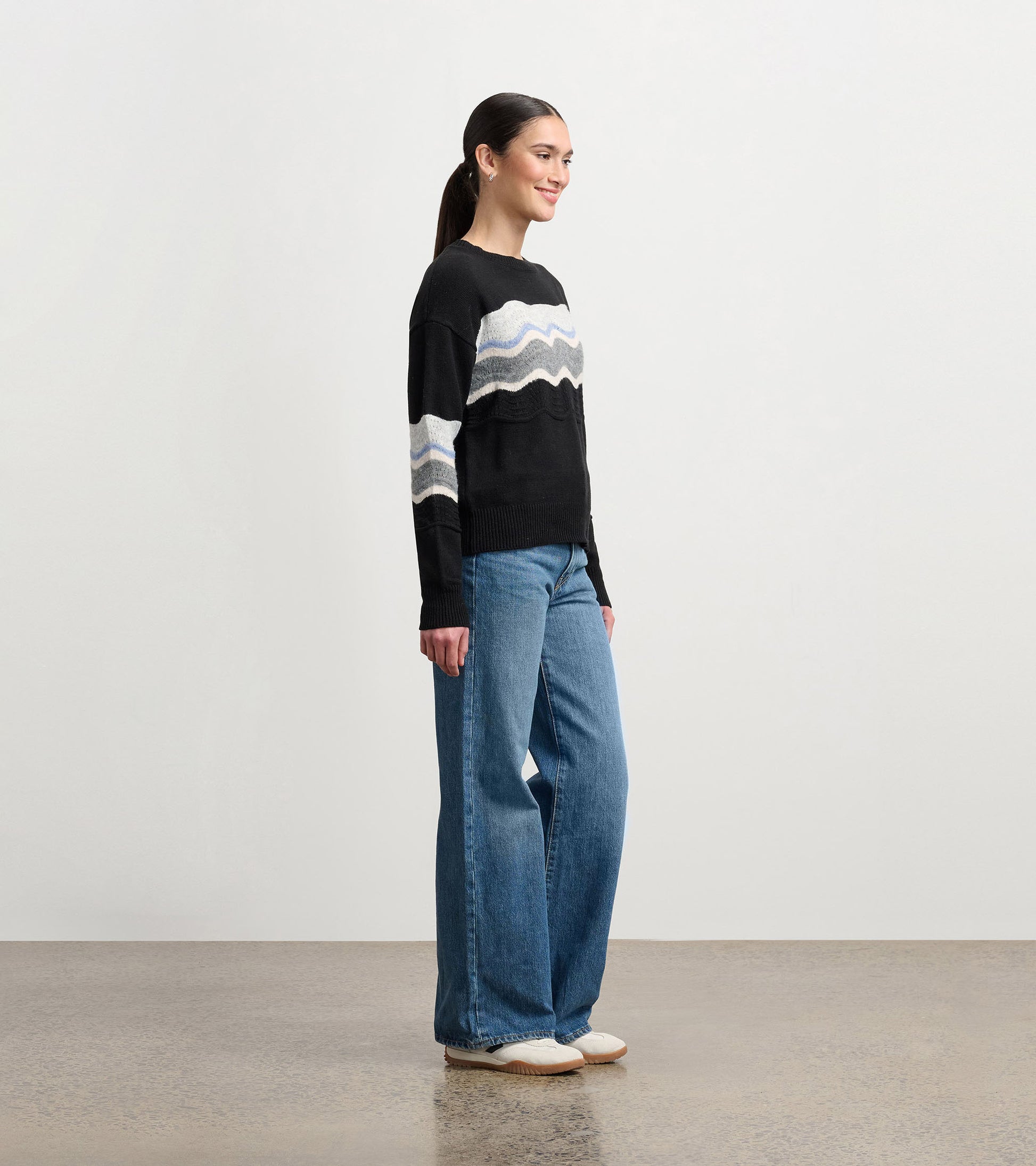 Black pointelle sweater featuring a wavy pattern in gray and blue, styled with wide-leg jeans.