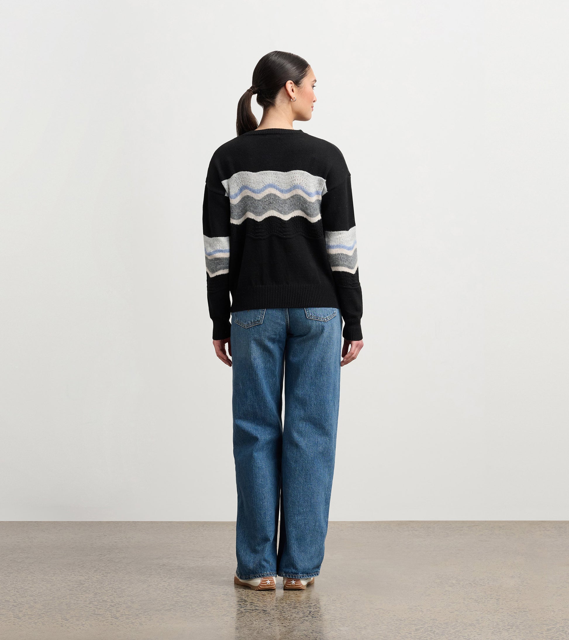 Black pointelle sweater featuring a wavy pattern in gray and blue, styled with loose blue jeans.