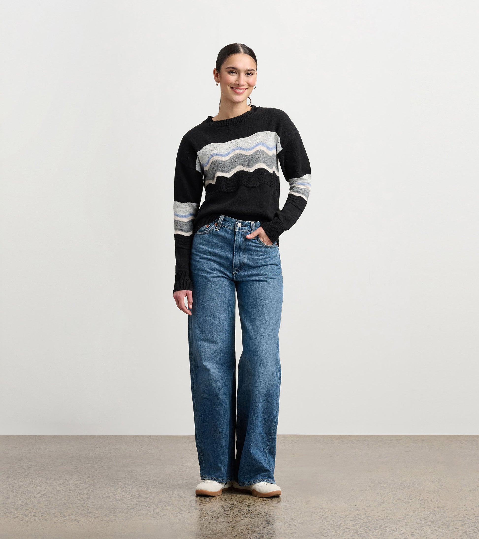 Black pointelle sweater featuring a wavy pattern in gray and blue, styled with high-waisted jeans.