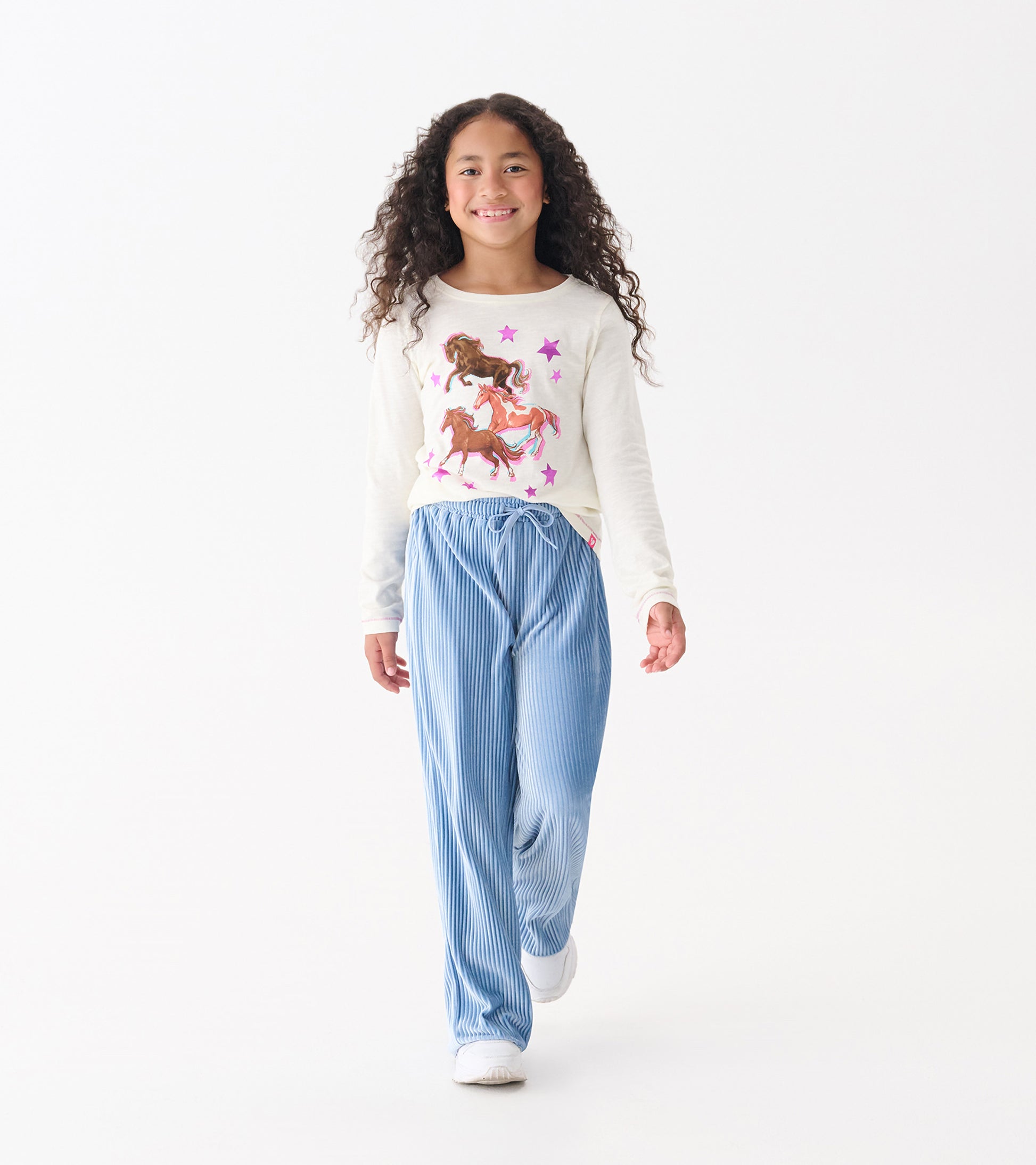 Long sleeve cream tee featuring colorful galloping horses and stars, paired with blue striped pants.
