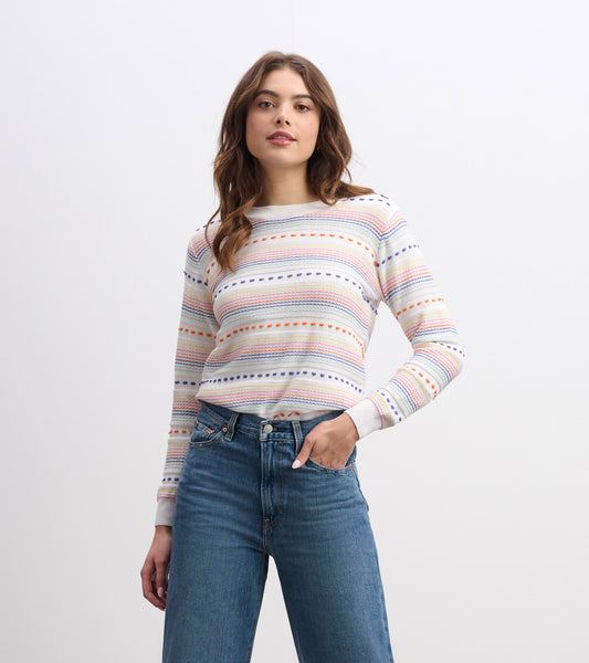 Striped long-sleeve sweater in cream with multicolored lines, paired with high-waisted jeans.