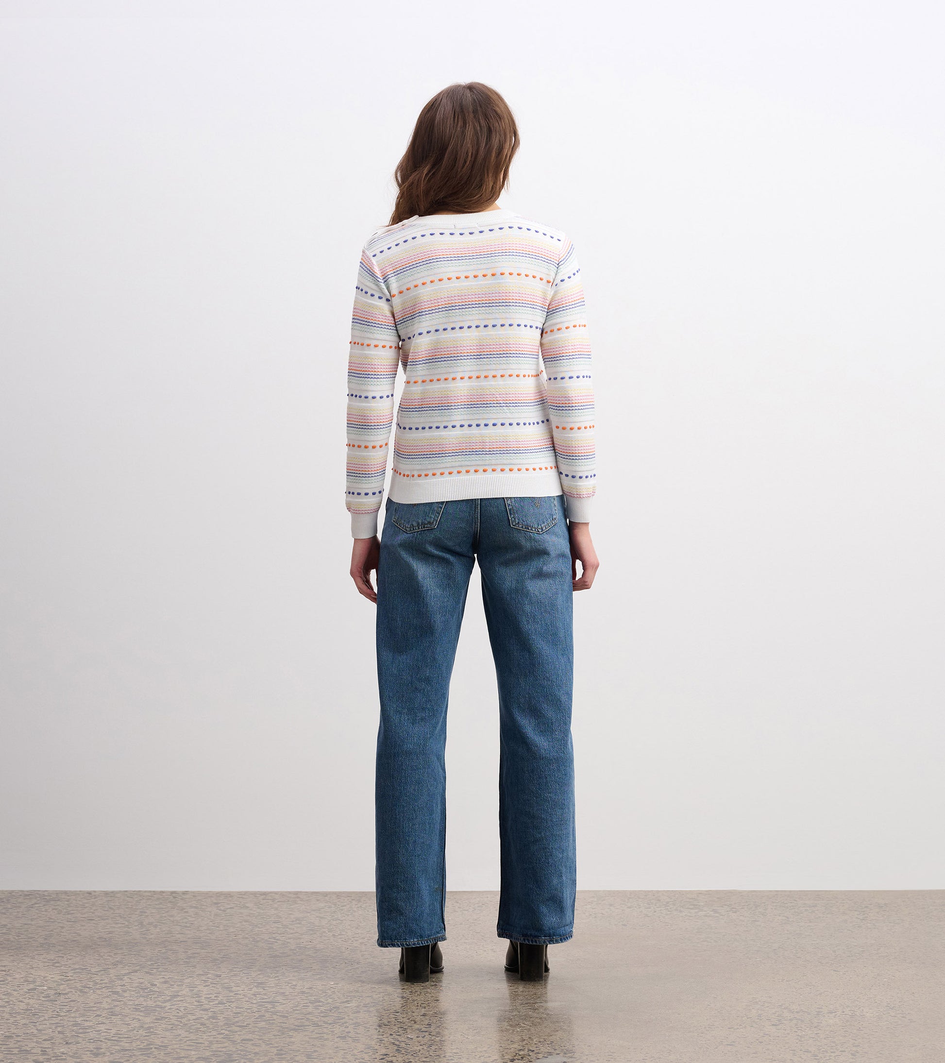 Back view of a lightweight, multicolored striped sweater paired with blue jeans.