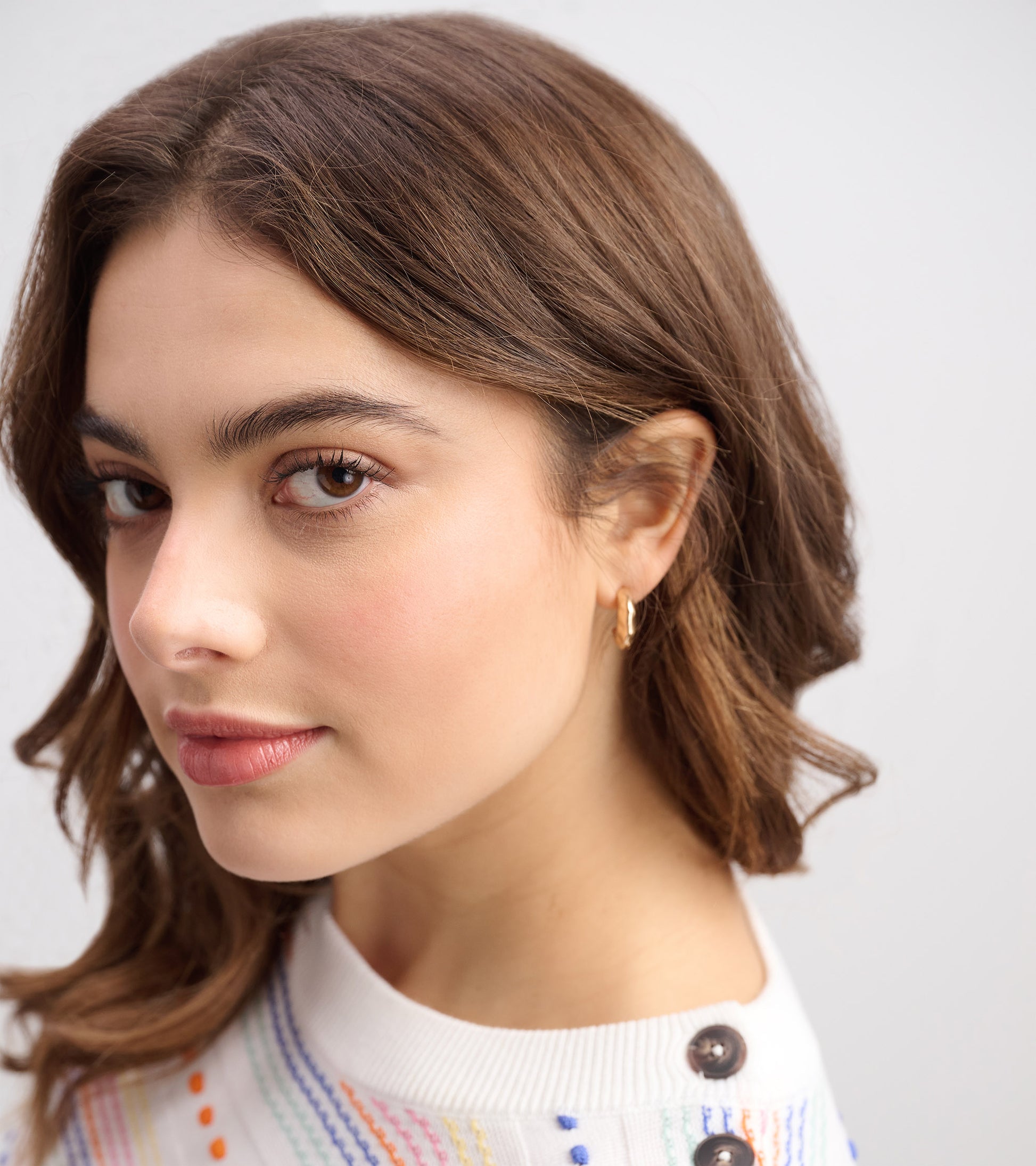 Close-up of a model wearing a white sweater with colorful stripes and button details, showcasing a casual style.
