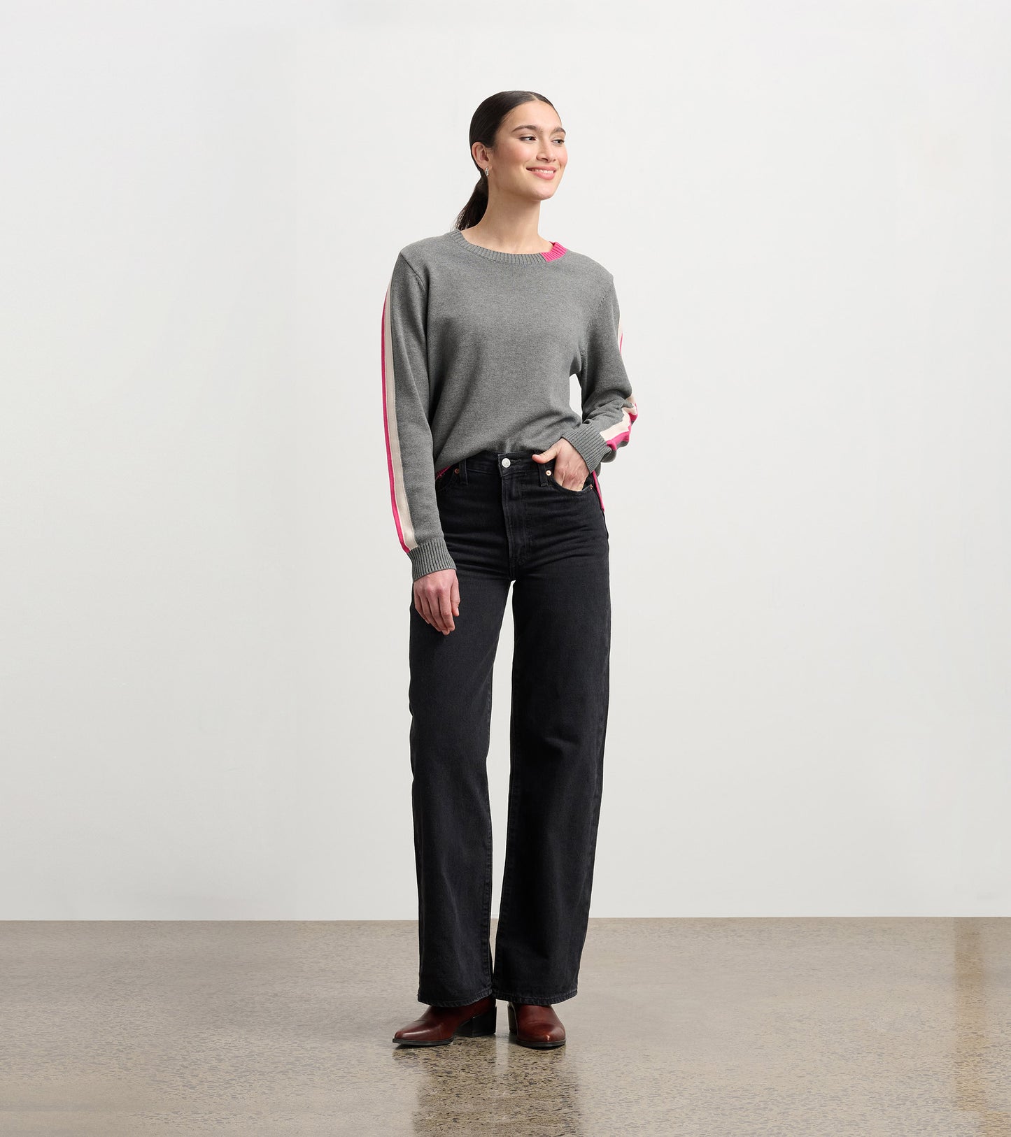Charcoal sweater with contrast pink trim, long sleeves, and a relaxed fit, styled with high-waisted black jeans.