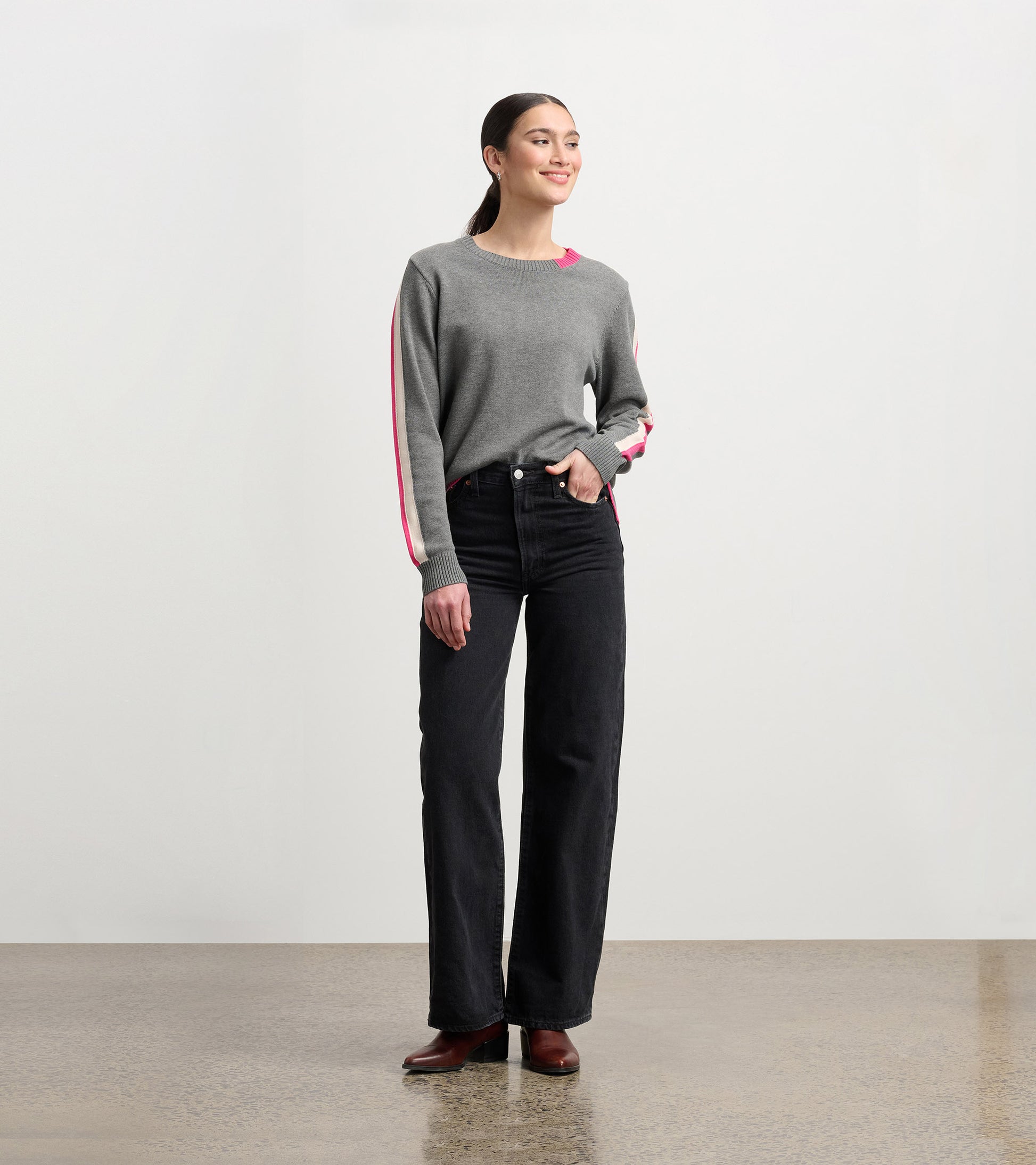 Charcoal sweater with contrast pink trim, long sleeves, and a relaxed fit, styled with high-waisted black jeans.