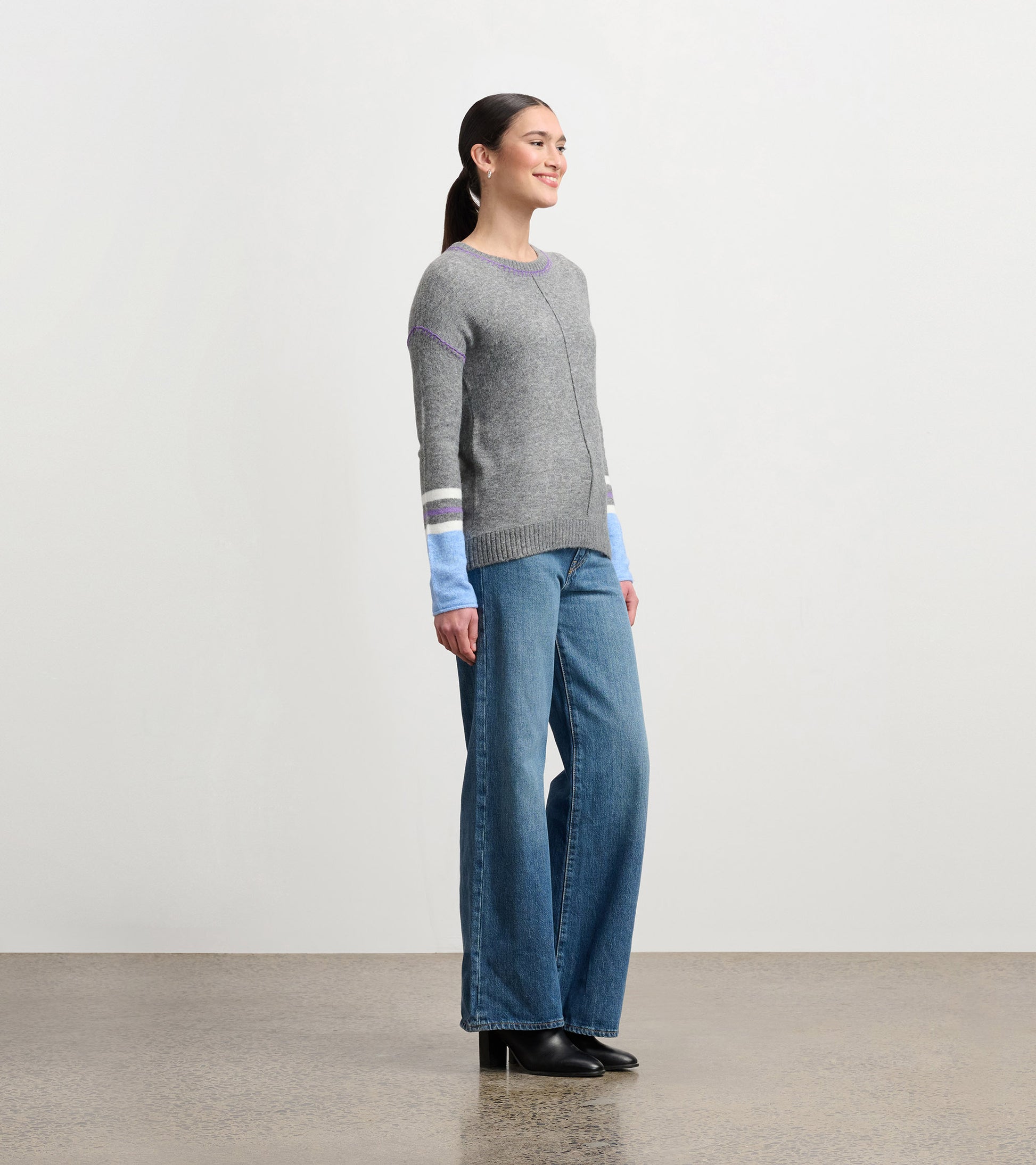 Charcoal melange sweater with colorful striped sleeves, paired with wide-leg jeans and heeled boots, shown from the side.