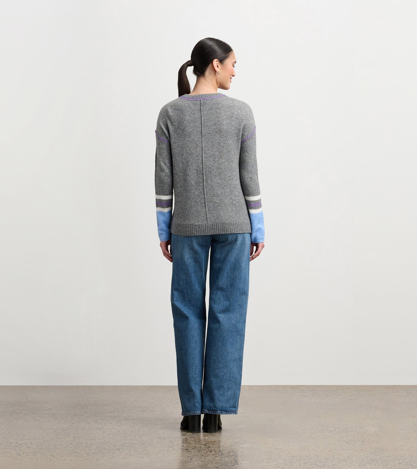Charcoal melange sweater with colorful striped sleeves, featuring a relaxed fit and ribbed hem, worn with wide-leg jeans.