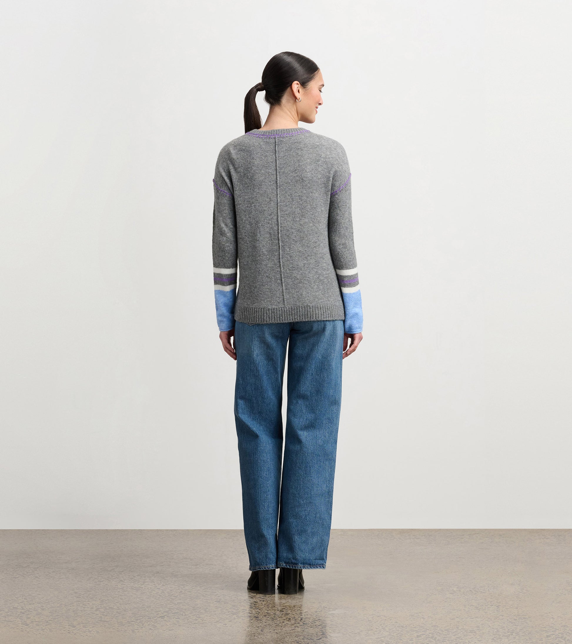 Charcoal melange sweater with colorful striped sleeves, featuring a relaxed fit and ribbed hem, worn with wide-leg jeans.