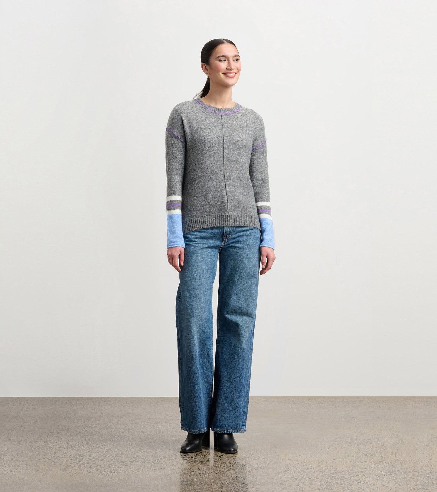 Charcoal melange sweater with colorful striped sleeves, round neckline, and a relaxed fit, worn with wide-leg jeans.