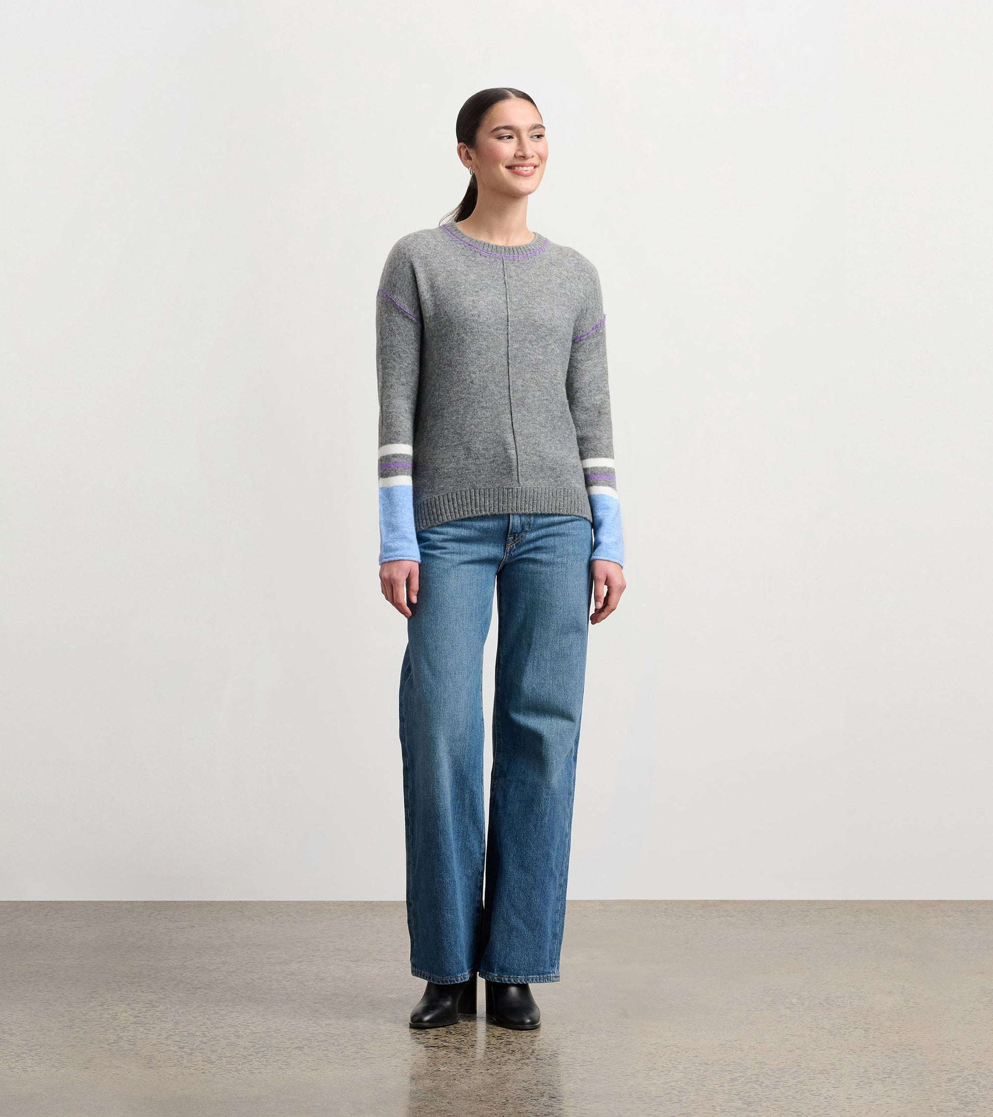 Charcoal melange sweater with colorful striped sleeves, round neckline, and a relaxed fit, worn with wide-leg jeans.