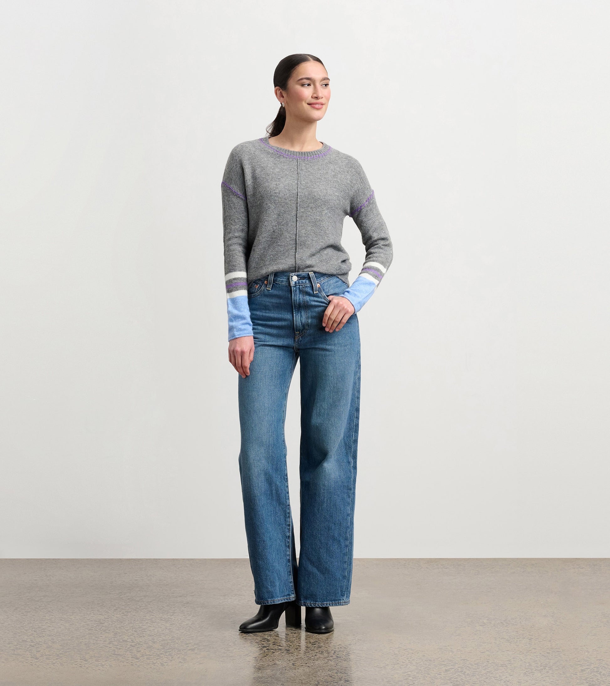 Charcoal melange sweater with contrasting blue and purple striped sleeves, styled with high-waisted jeans.
