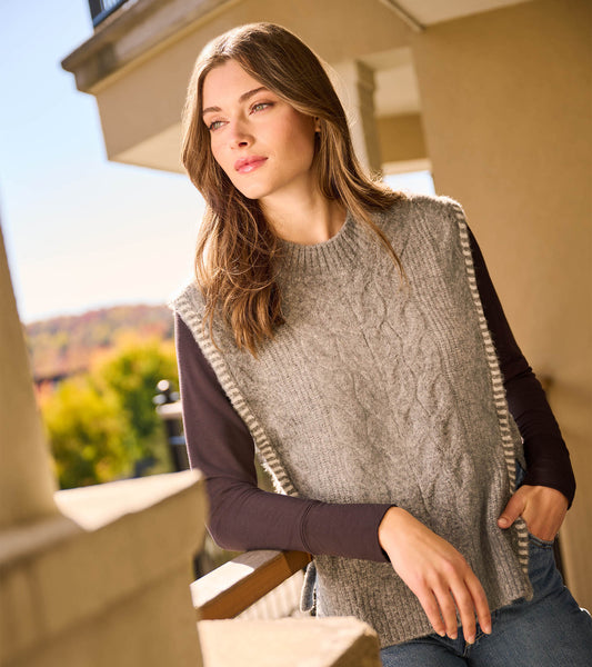 Charcoal melange side-tie sweater vest with cable knit pattern, worn over a long-sleeve top, featuring a relaxed fit.