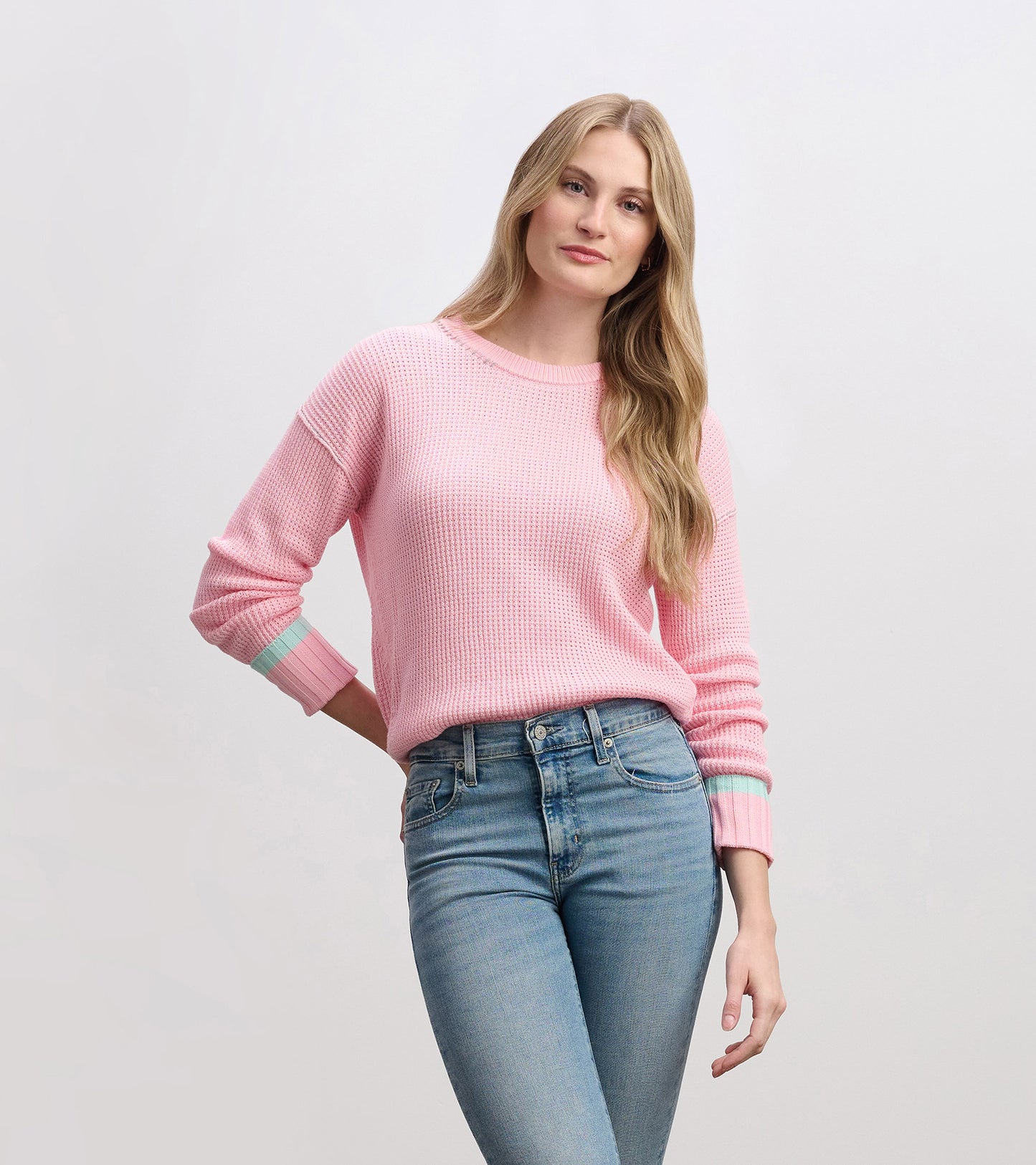 Fuchsia pink waffle knit sweater with contrasting mint green cuffs, styled with high-waisted jeans.