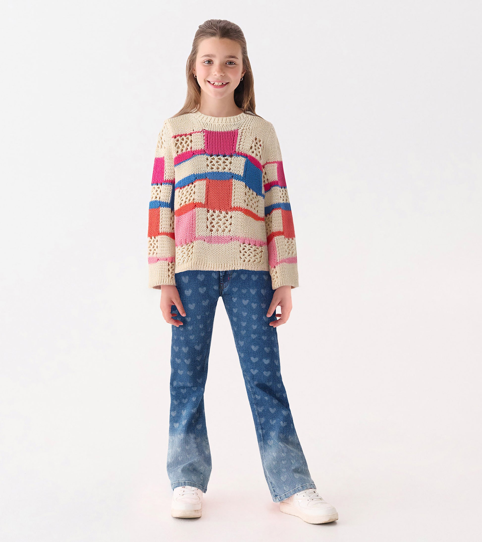 Knit sweater featuring a mix of colorful patterns, paired with heart-print jeans and white sneakers.