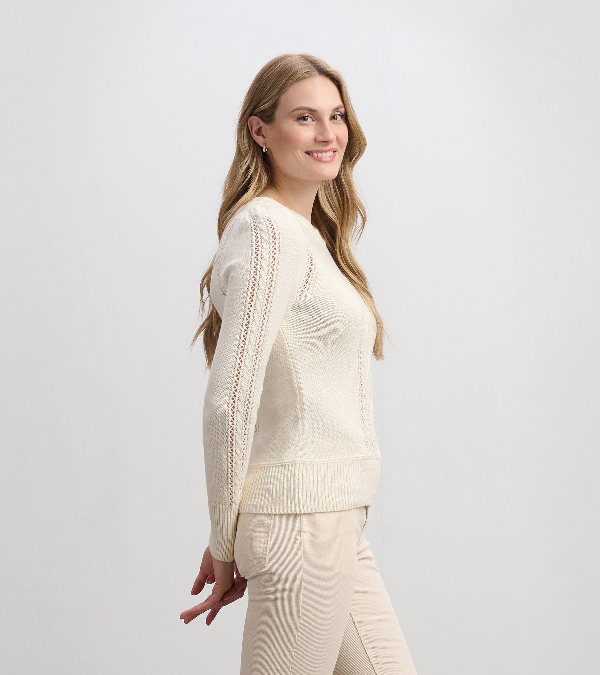 Cream sweater featuring a fitted silhouette and lace detailing on the sleeves, styled with light-colored pants.