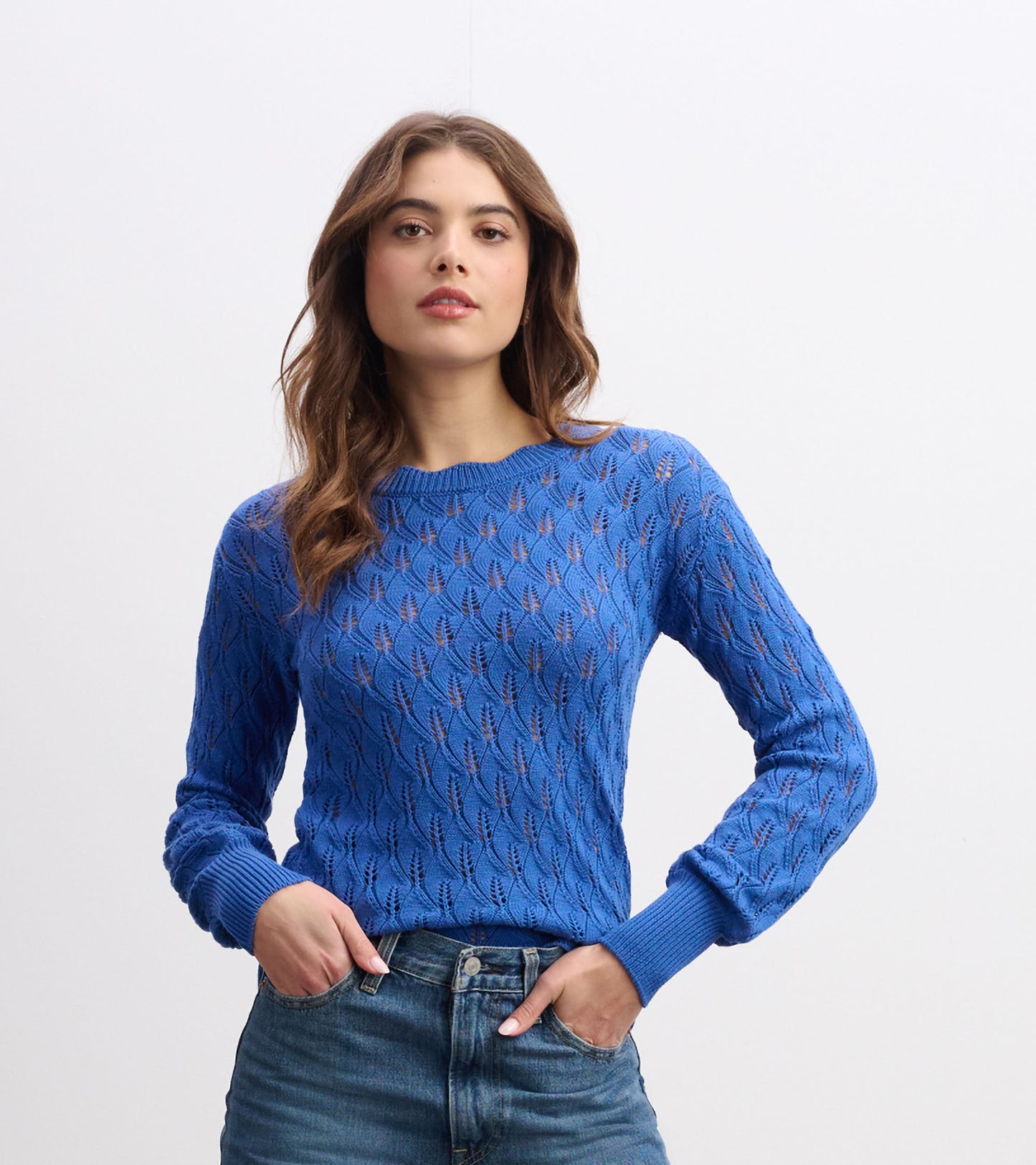 Denim blue sweater with a textured leaf pattern and ribbed cuffs, styled with high-waisted jeans.