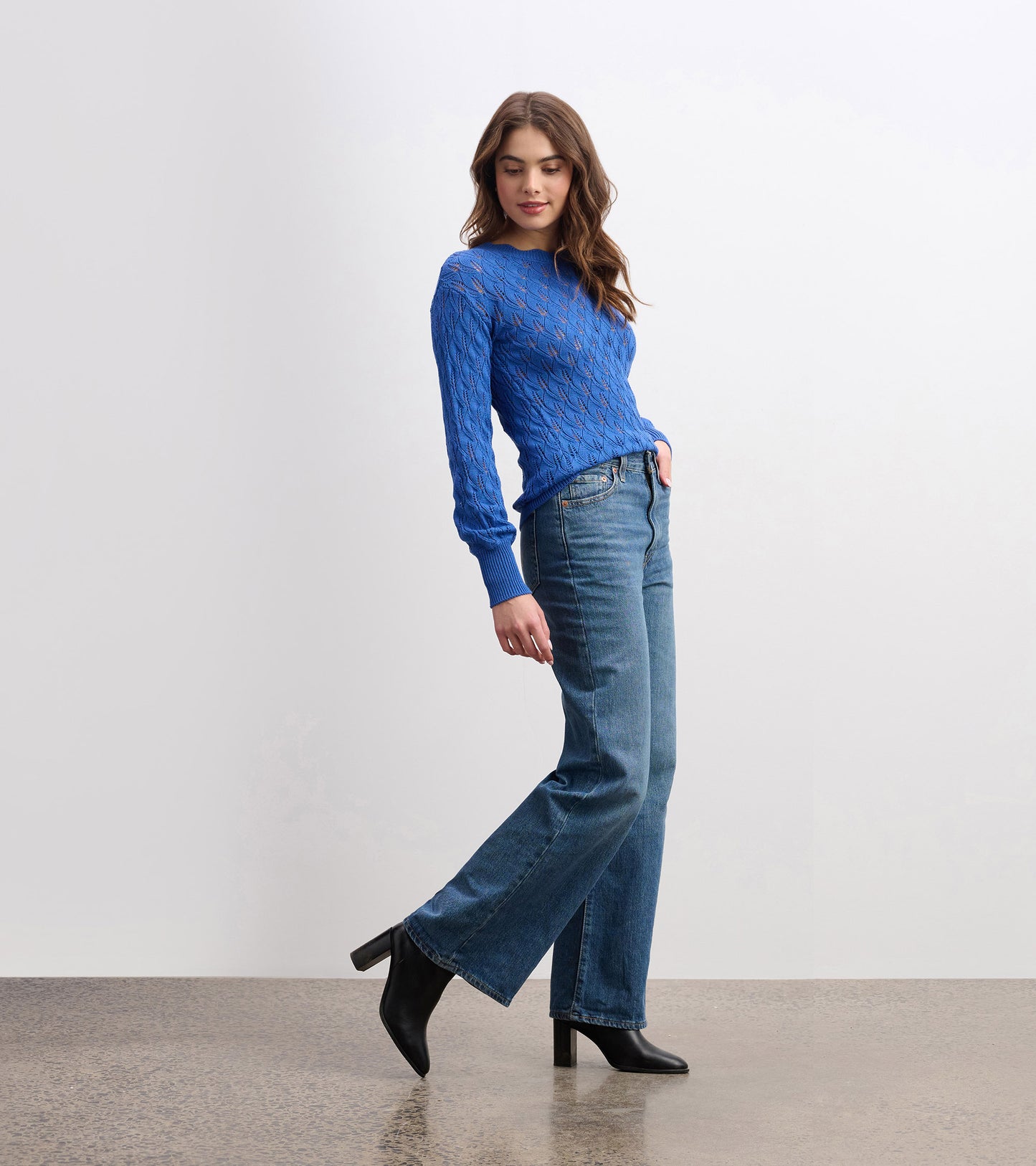 Denim blue sweater with a textured pattern and long sleeves, styled with high-waisted jeans and heeled boots.