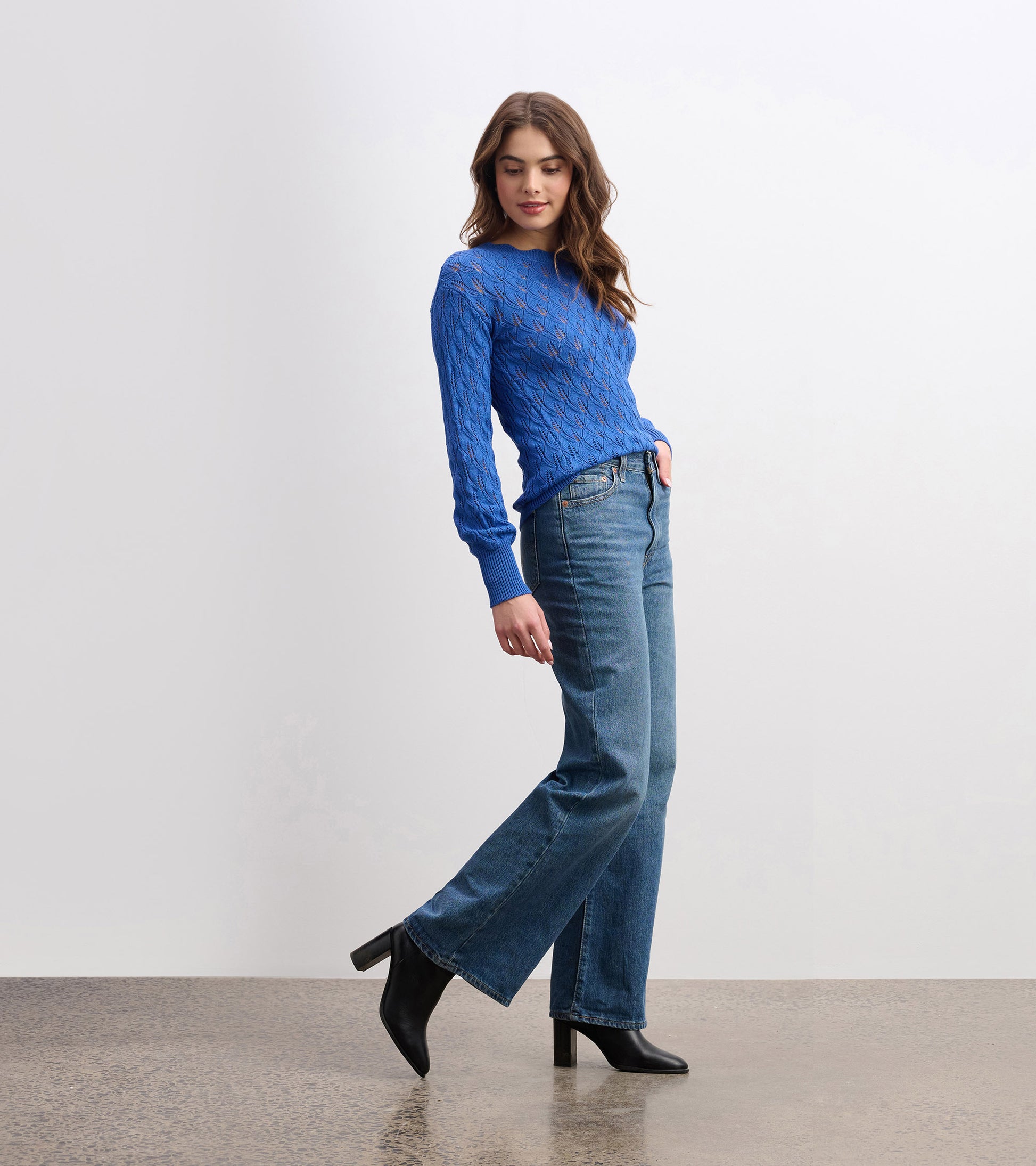 Denim blue sweater with a textured pattern and long sleeves, styled with high-waisted jeans and heeled boots.