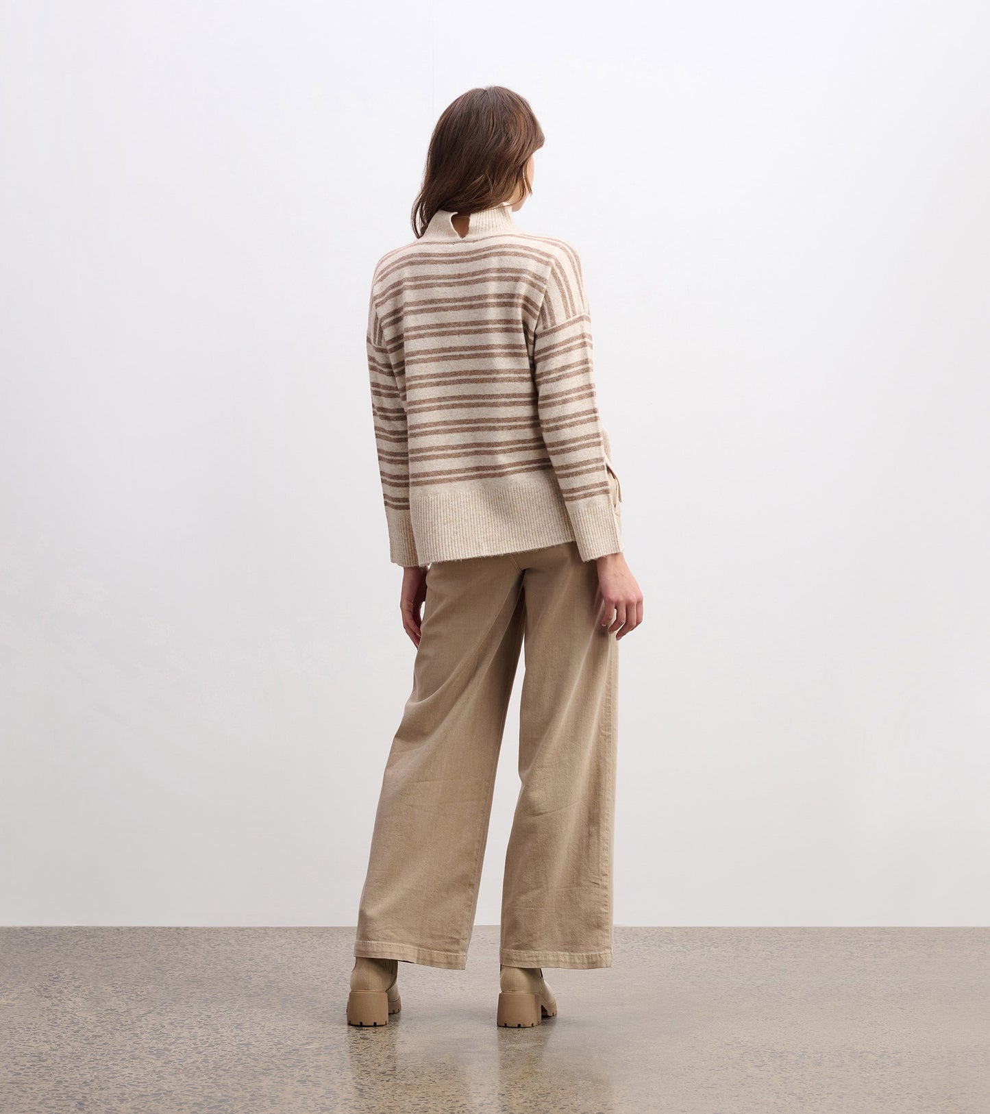 Mock neck sweater in camel with double stripes, featuring a relaxed fit and ribbed hem, styled with beige wide-leg pants.
