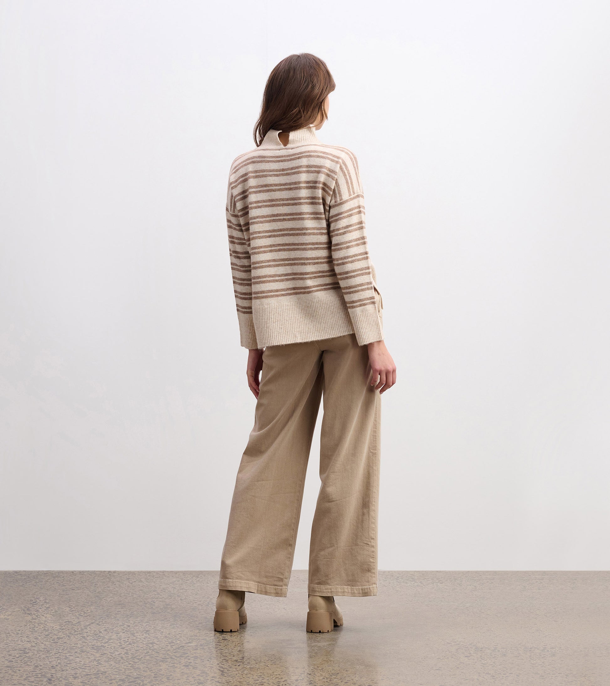 Mock neck sweater in camel with double stripes, featuring a relaxed fit and ribbed hem, styled with beige wide-leg pants.