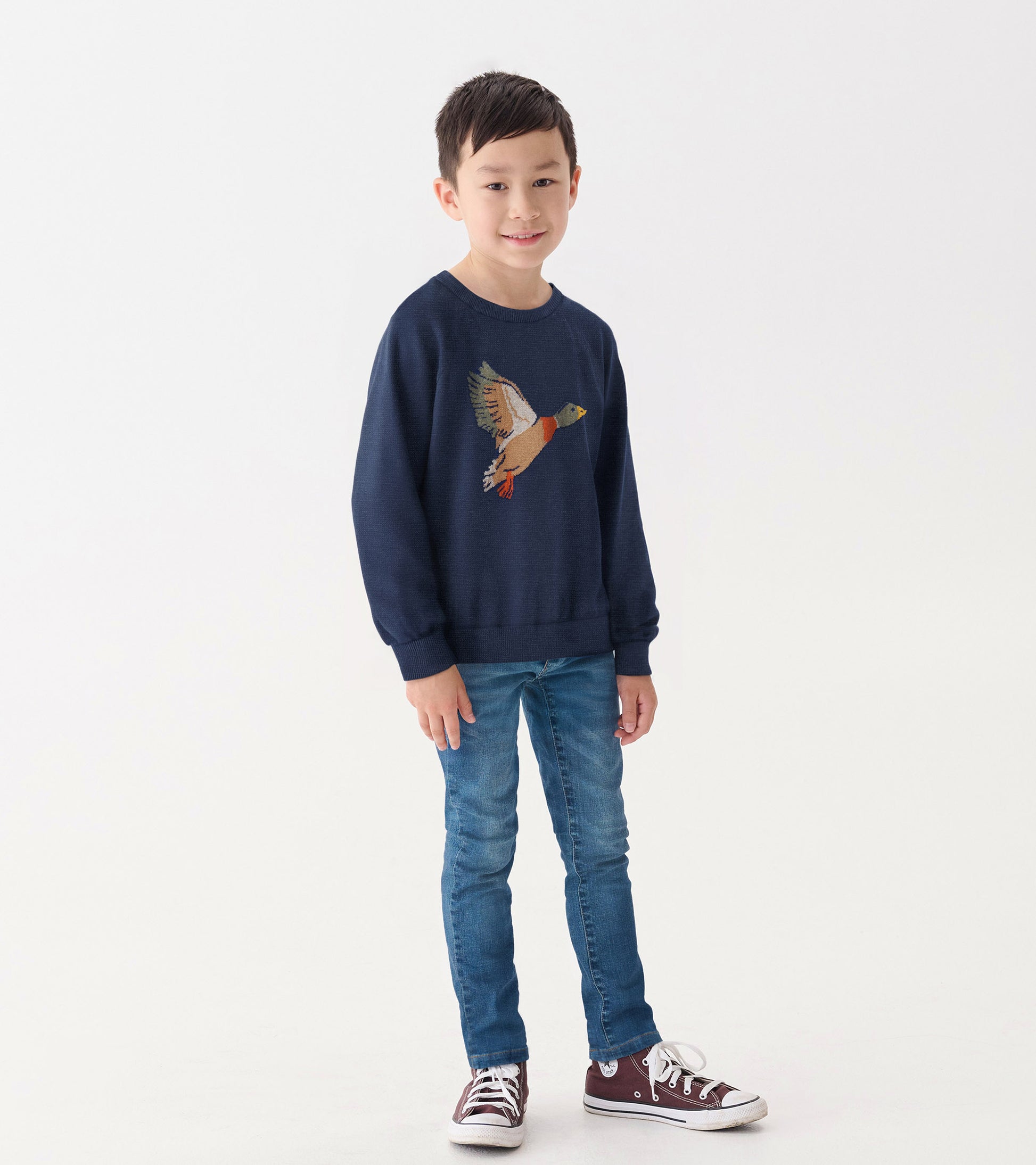 Navy crew neck sweater featuring a colorful duck design, worn by a boy with jeans and sneakers.