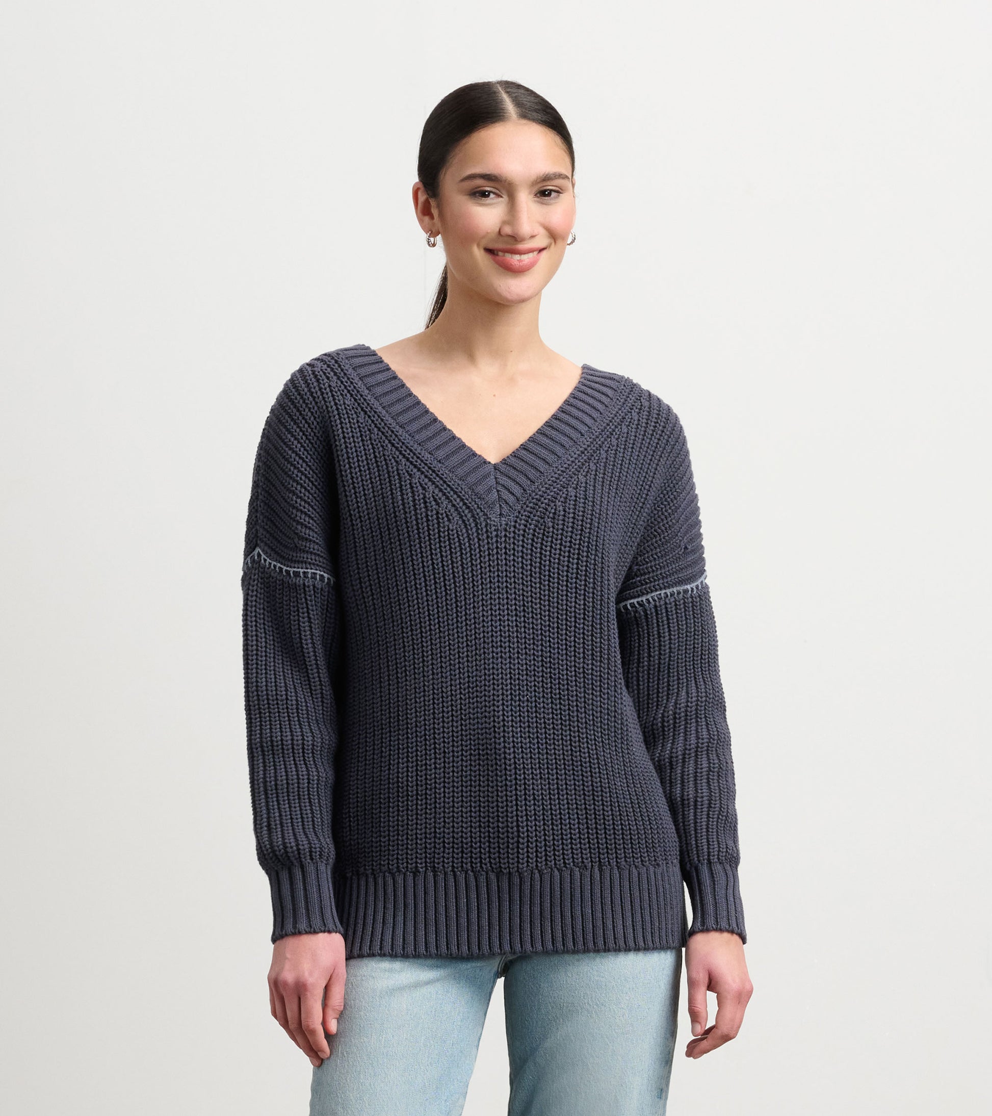Faded grey V-neck slouchy sweater with ribbed hem and textured knit, worn with light blue jeans.
