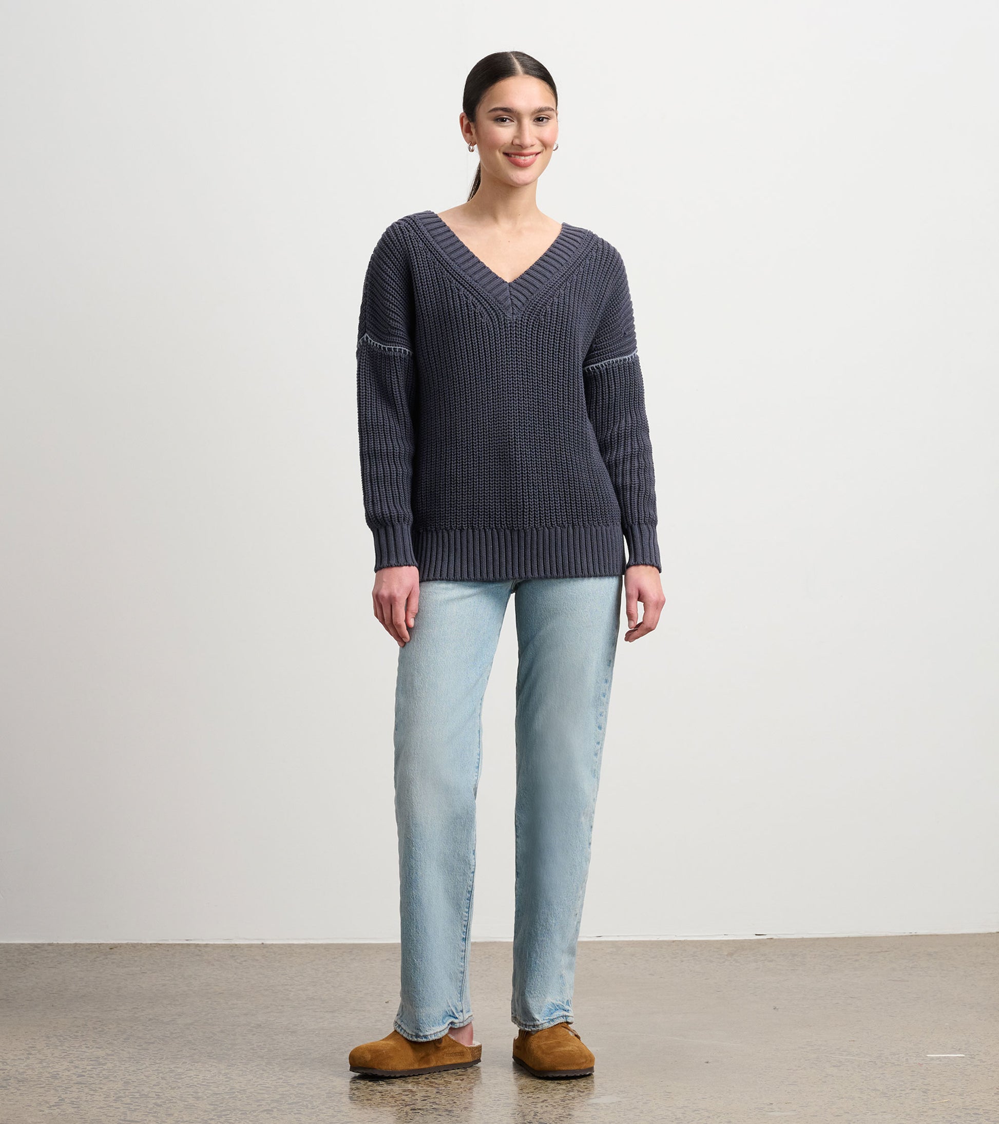 Faded grey V-neck slouchy sweater with ribbed cuffs and hem, styled with light blue jeans and brown clogs.