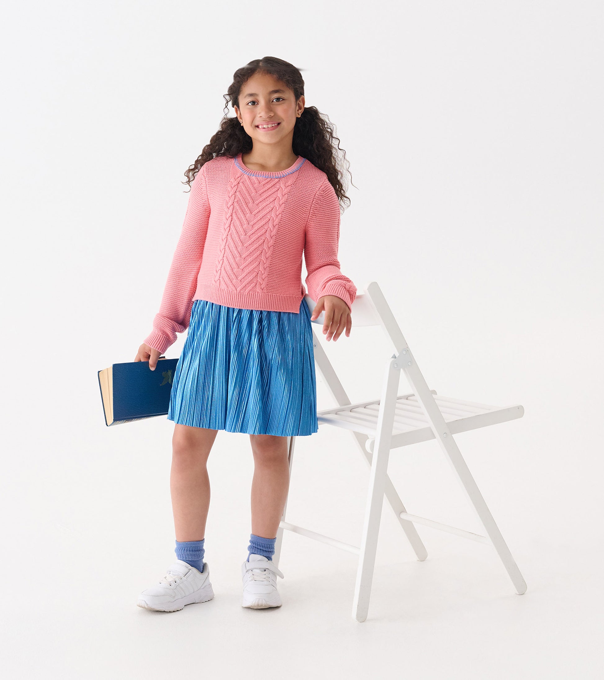 Flamingo pink sweater with textured pattern paired with a pleated blue skirt, worn by a girl holding a book.
