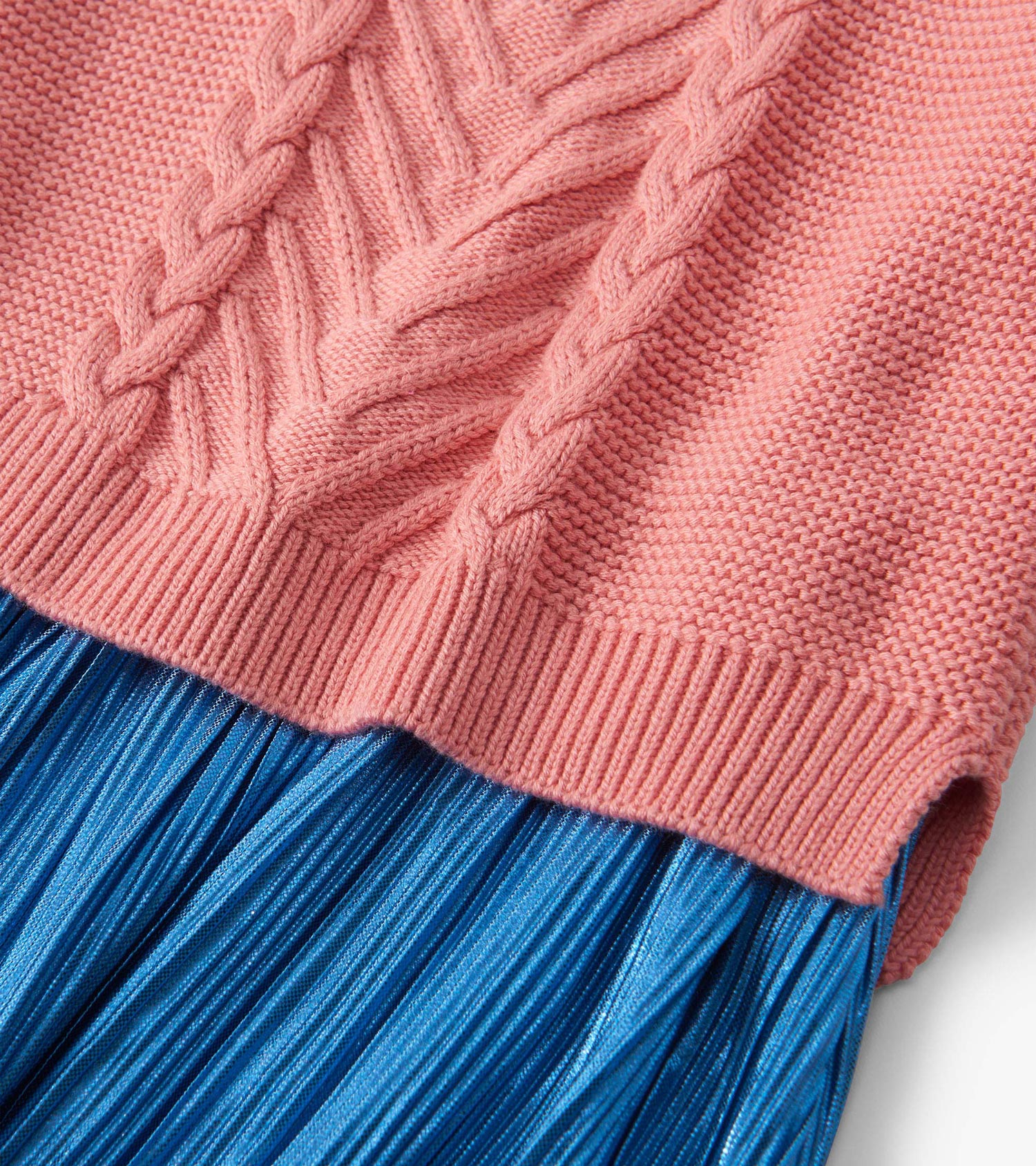 Flamingo pink knit top with braided texture and blue pleated skirt, showcasing a mix of materials and vibrant colors.