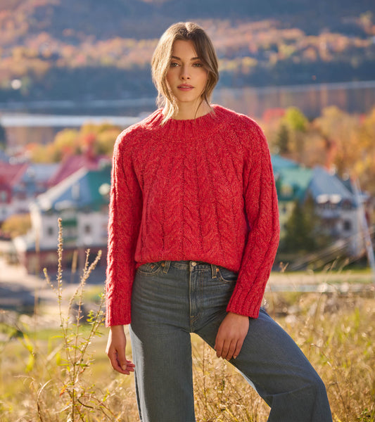 Red cable knit sweater with a round neckline, paired with wide-leg jeans and ankle boots.