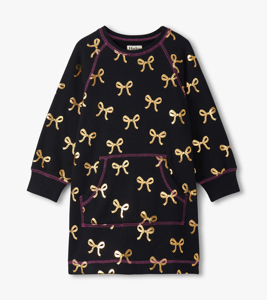 Black sweater dress featuring gold bow patterns and a front pocket, with purple stitching accents. Suitable for girls.