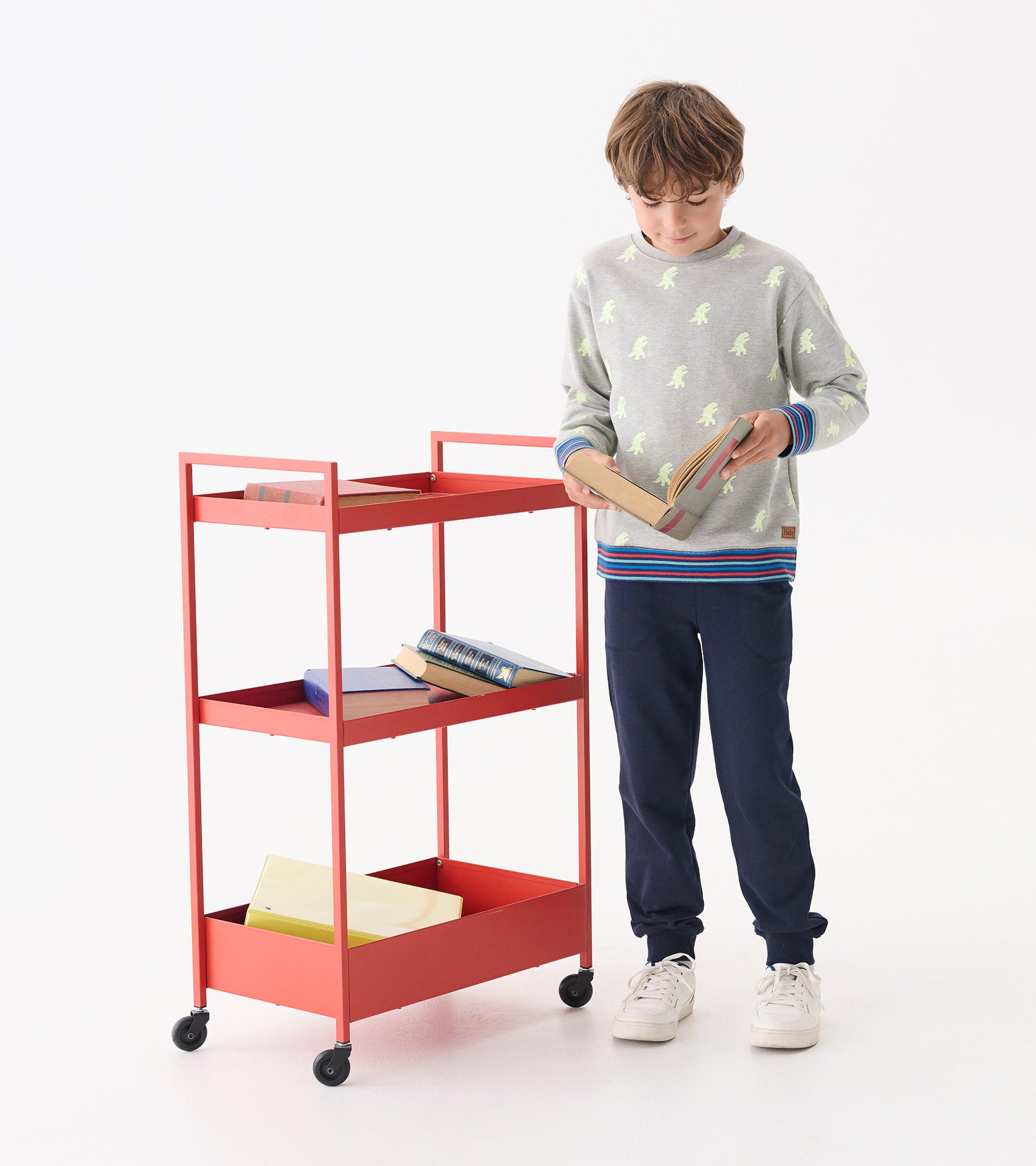 Gray pullover sweatshirt with green monster print, ribbed cuffs, worn by a boy holding a book near a red cart.